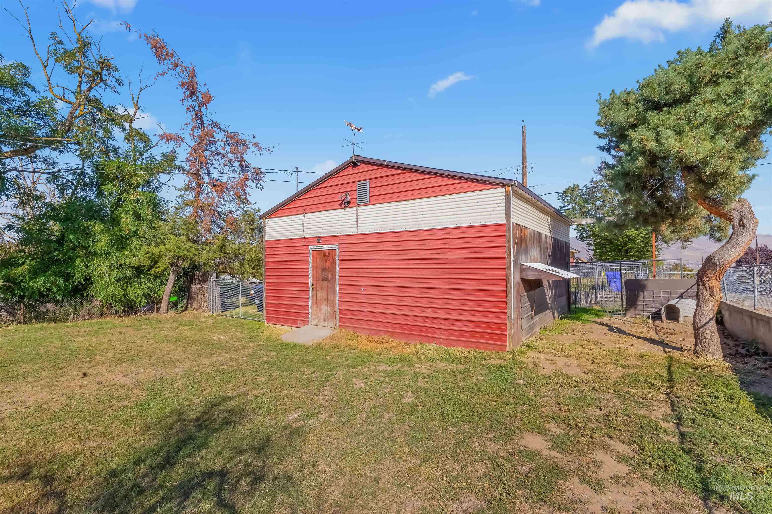 Red-and-white outbuilding with a weathered wooden door and a small lean-to in a fenced yard.