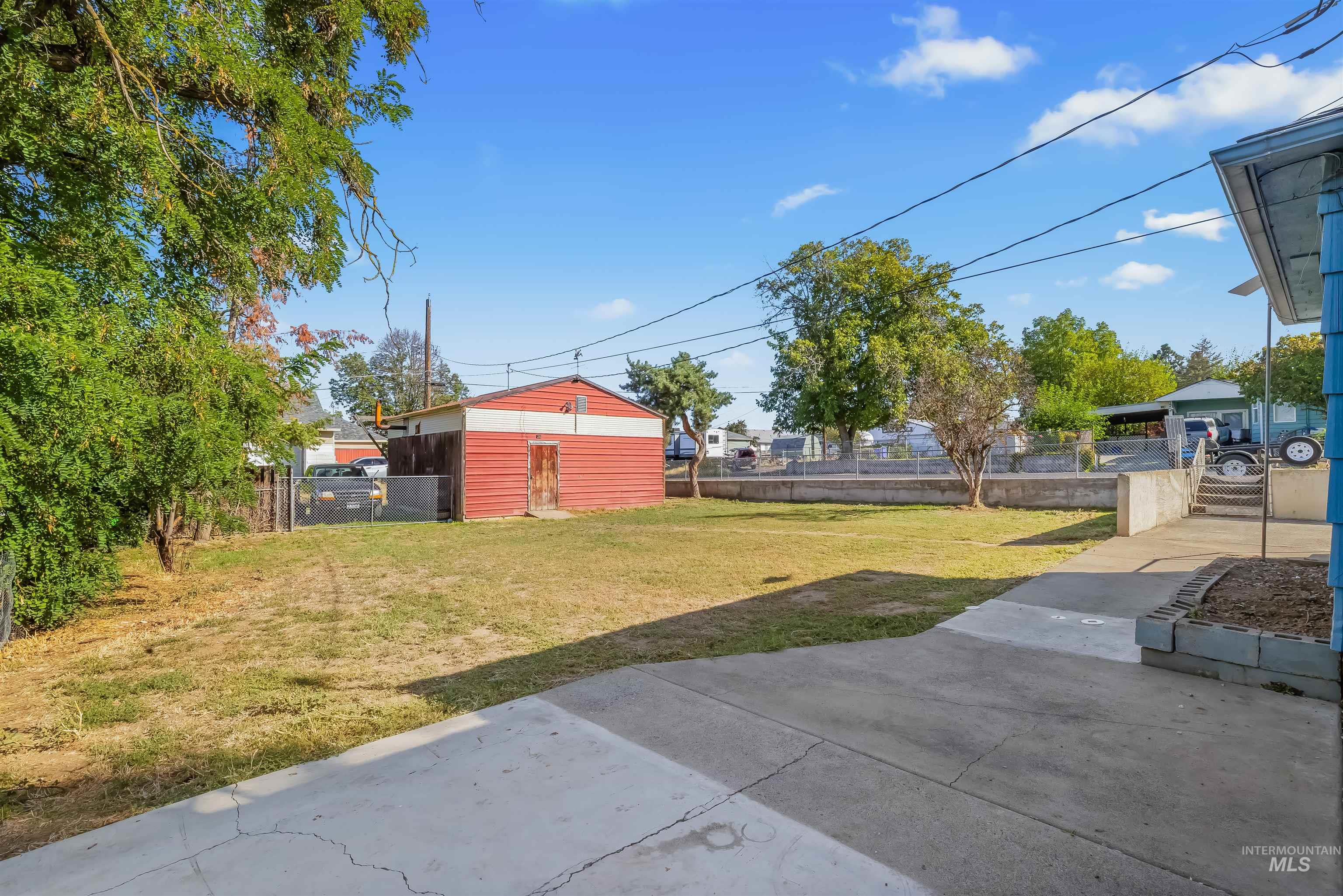 Backyard with a concrete patio, dry lawn, and red-and-white detached shed.