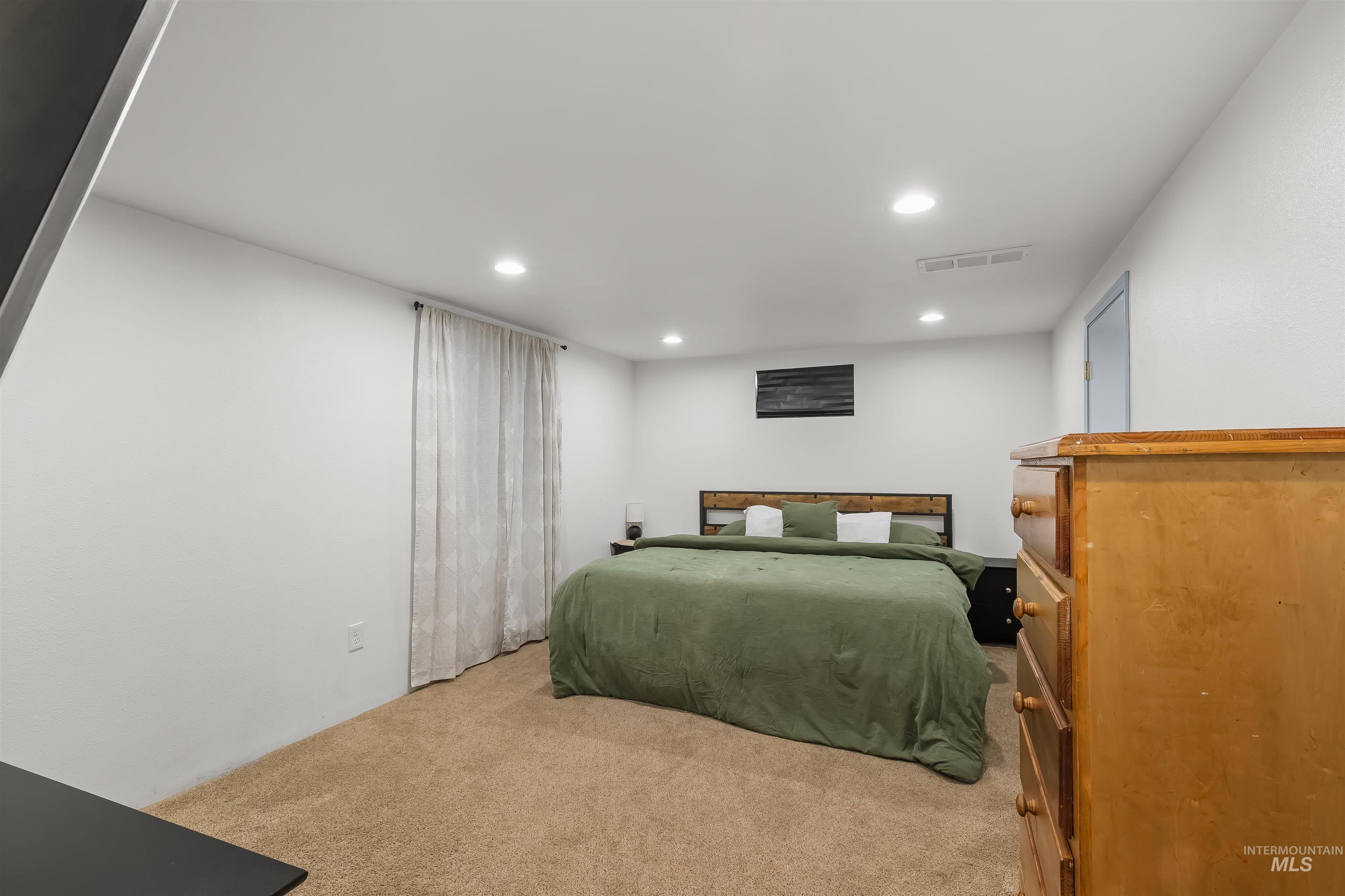 Bedroom with a green-covered bed, beige carpet, and a wooden dresser.