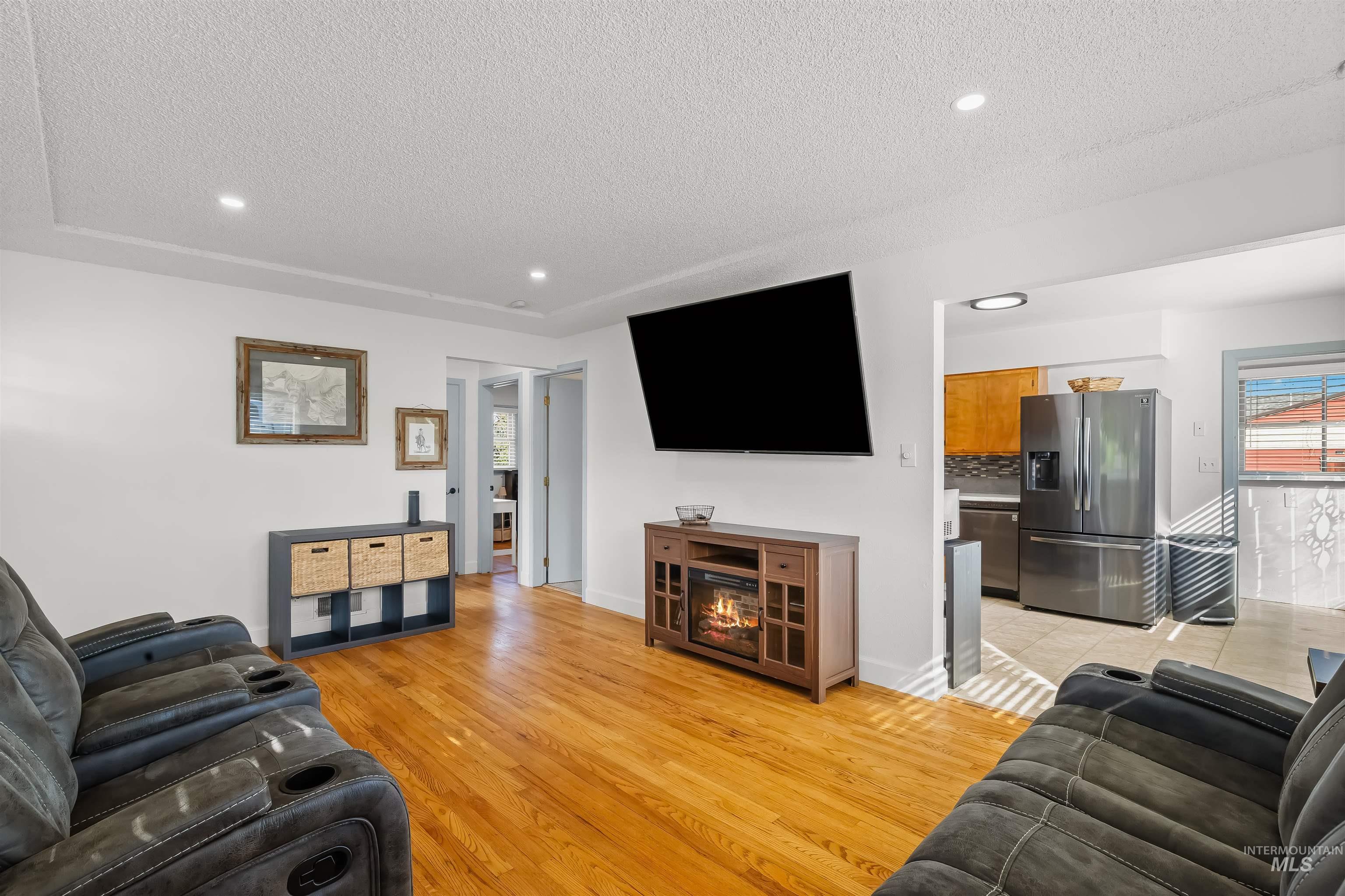 Living room with hardwood floors, reclining sofas, a wall-mounted television, and an electric fireplace.