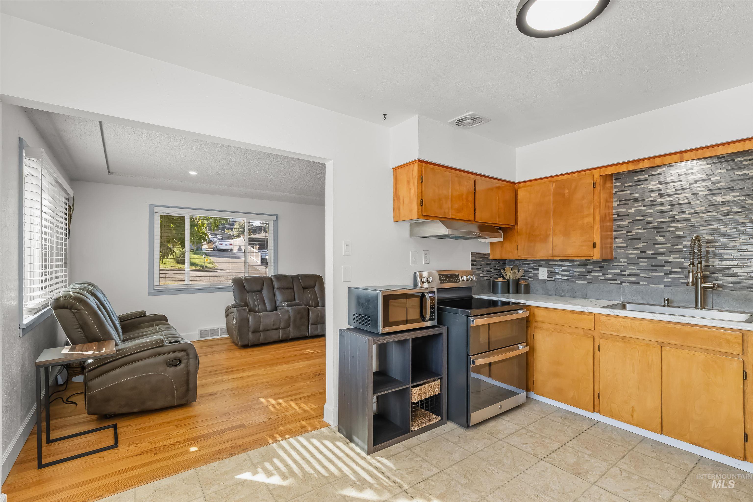 Kitchen opening to a living room, with warm wood cabinets, gray tile backsplash, and leather recliners.