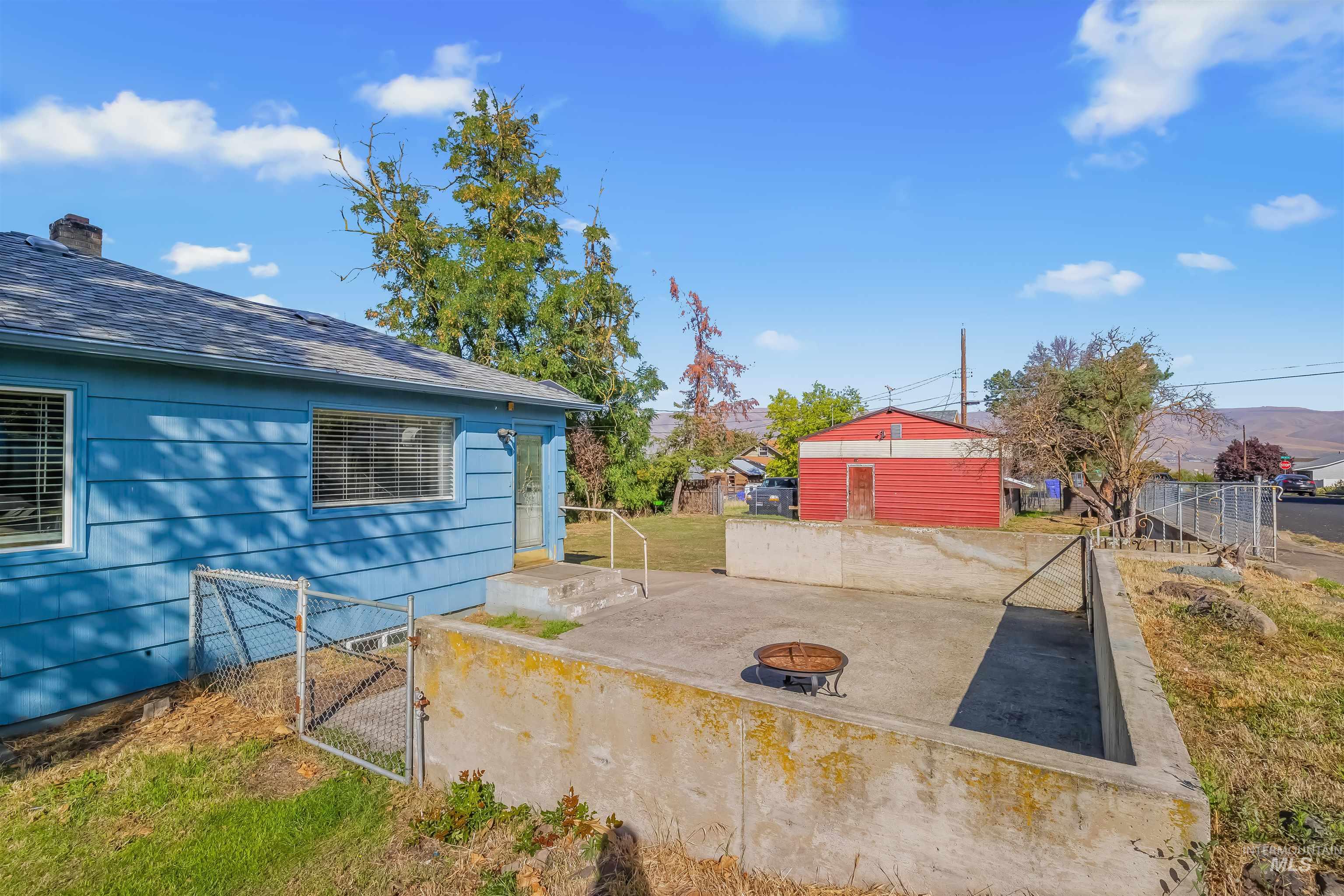 Blue-sided house beside a concrete patio with a fire pit and red detached shed.