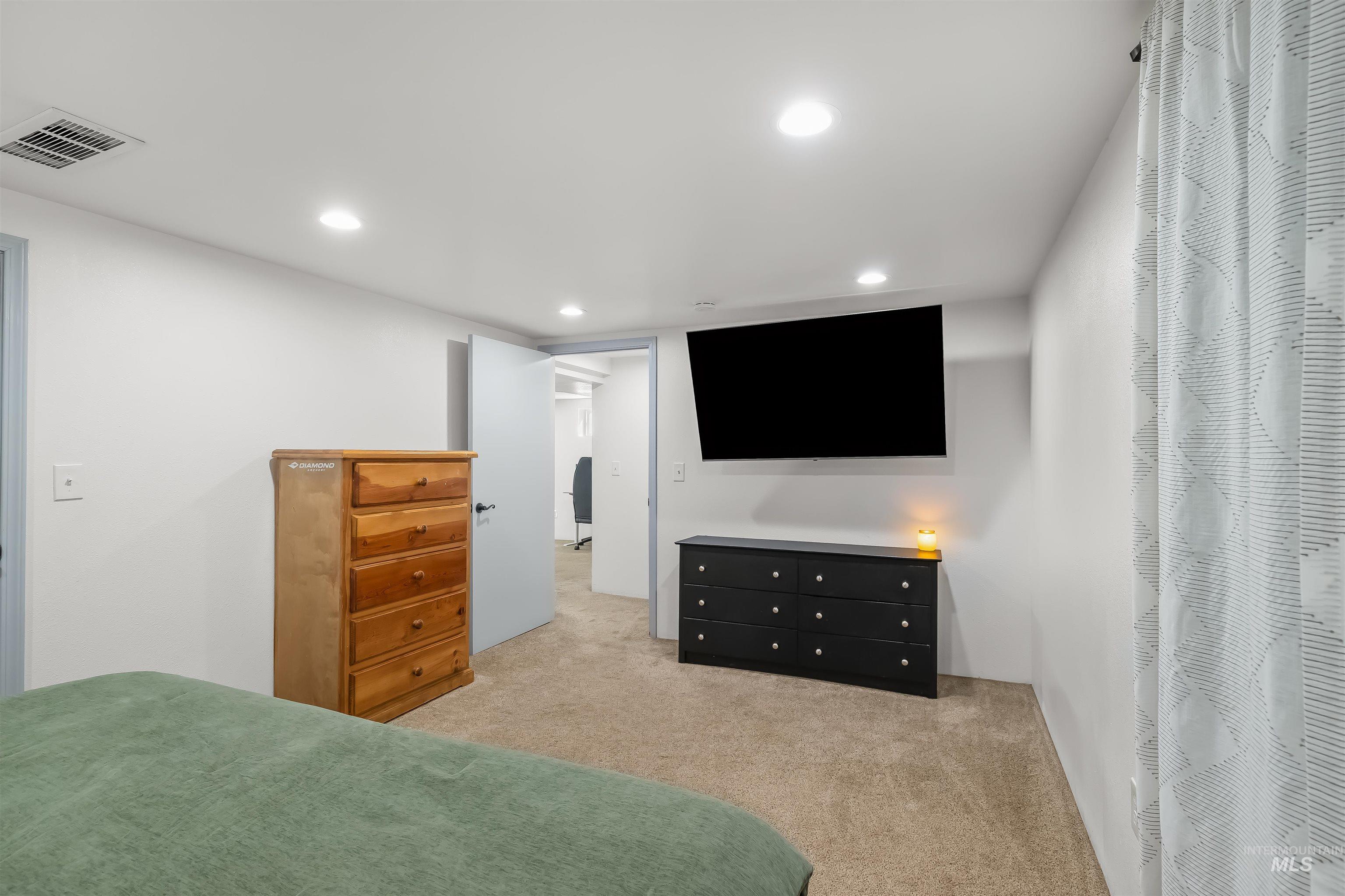 Furnished bedroom with a green bedspread, two dressers, and a wall-mounted television.
