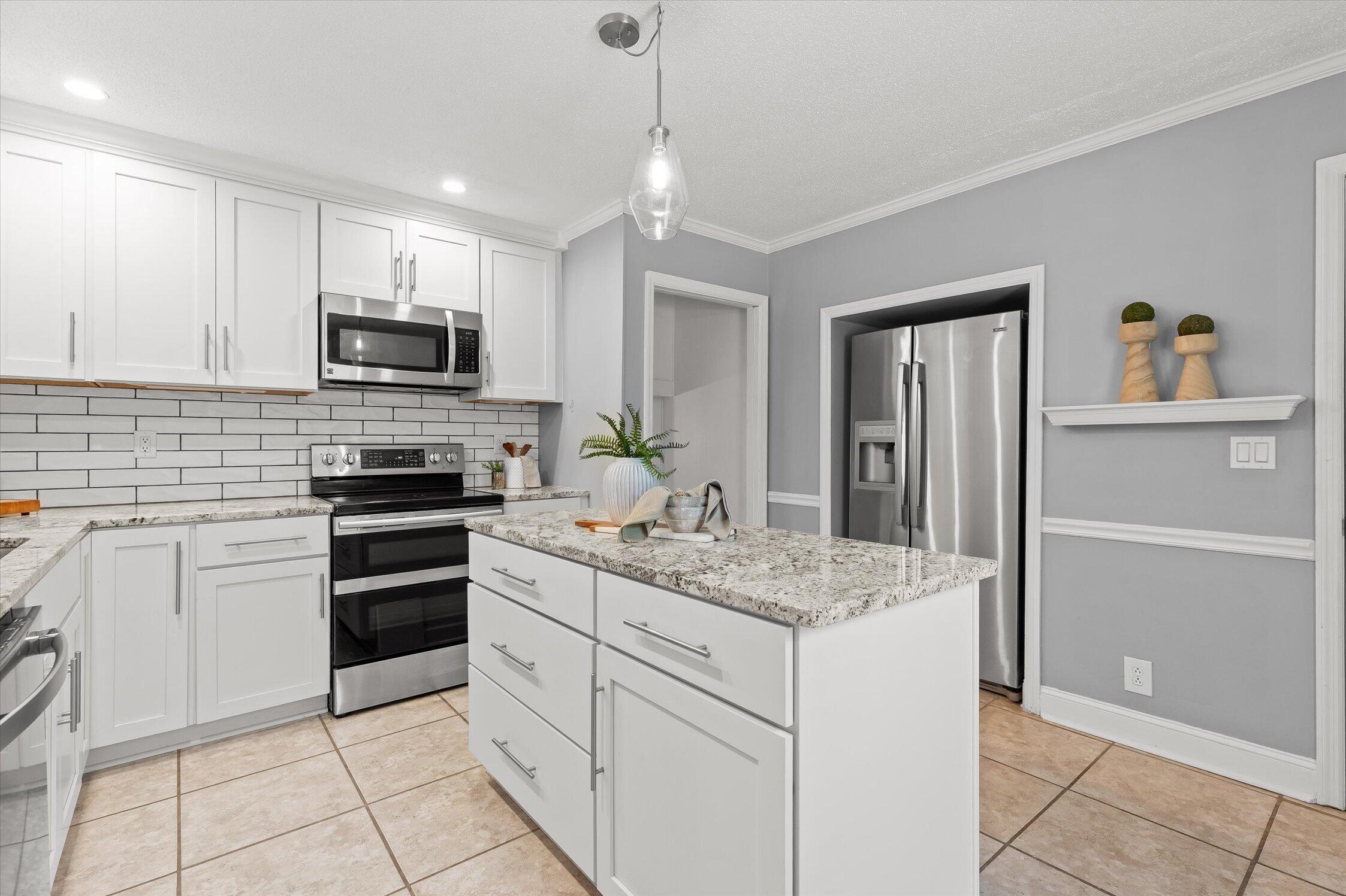Kitchen with a granite-topped island, white cabinets, and stainless steel appliances.