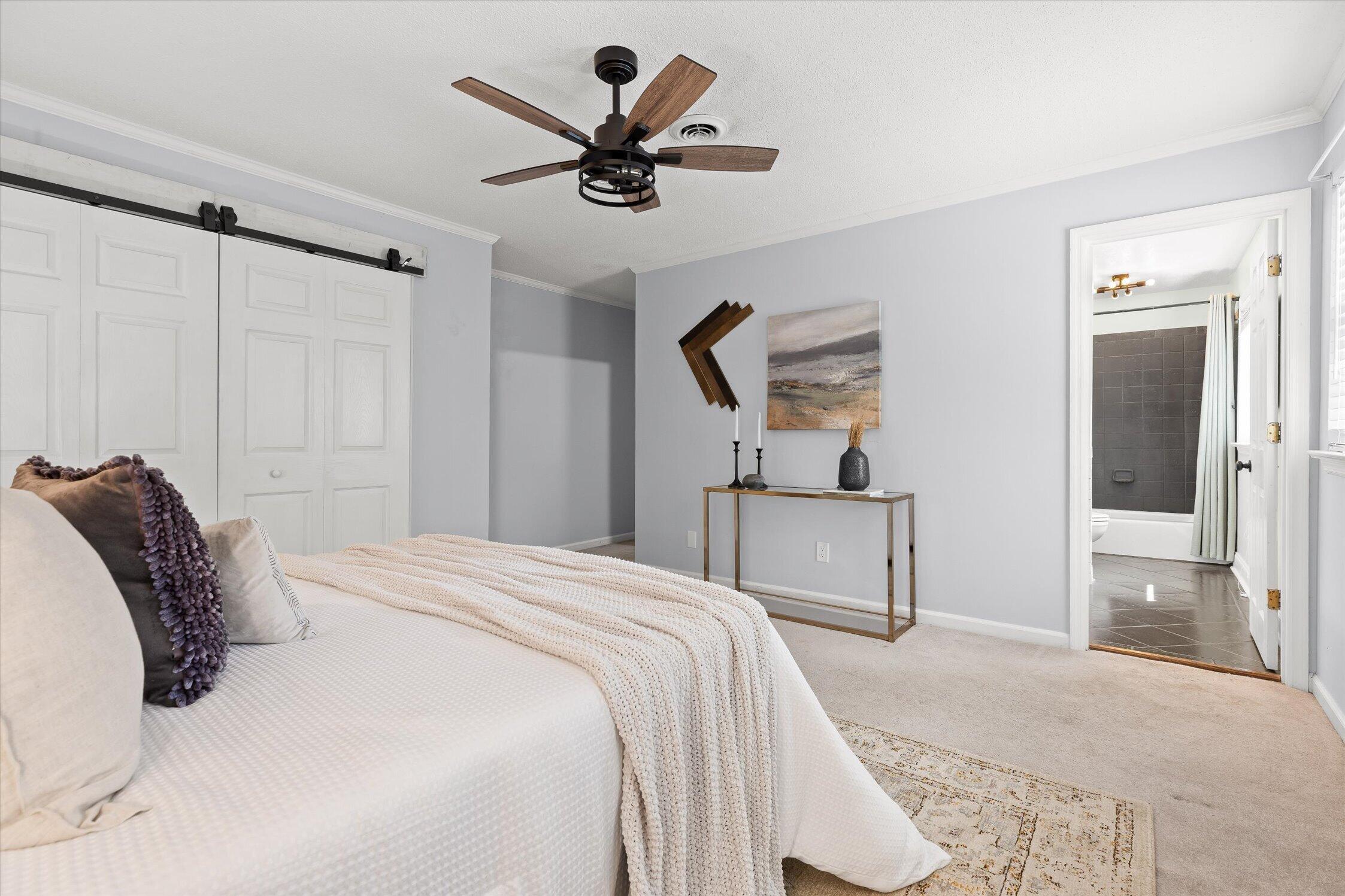 Bedroom with a white bed, sliding barn doors, and an ensuite bathroom doorway.