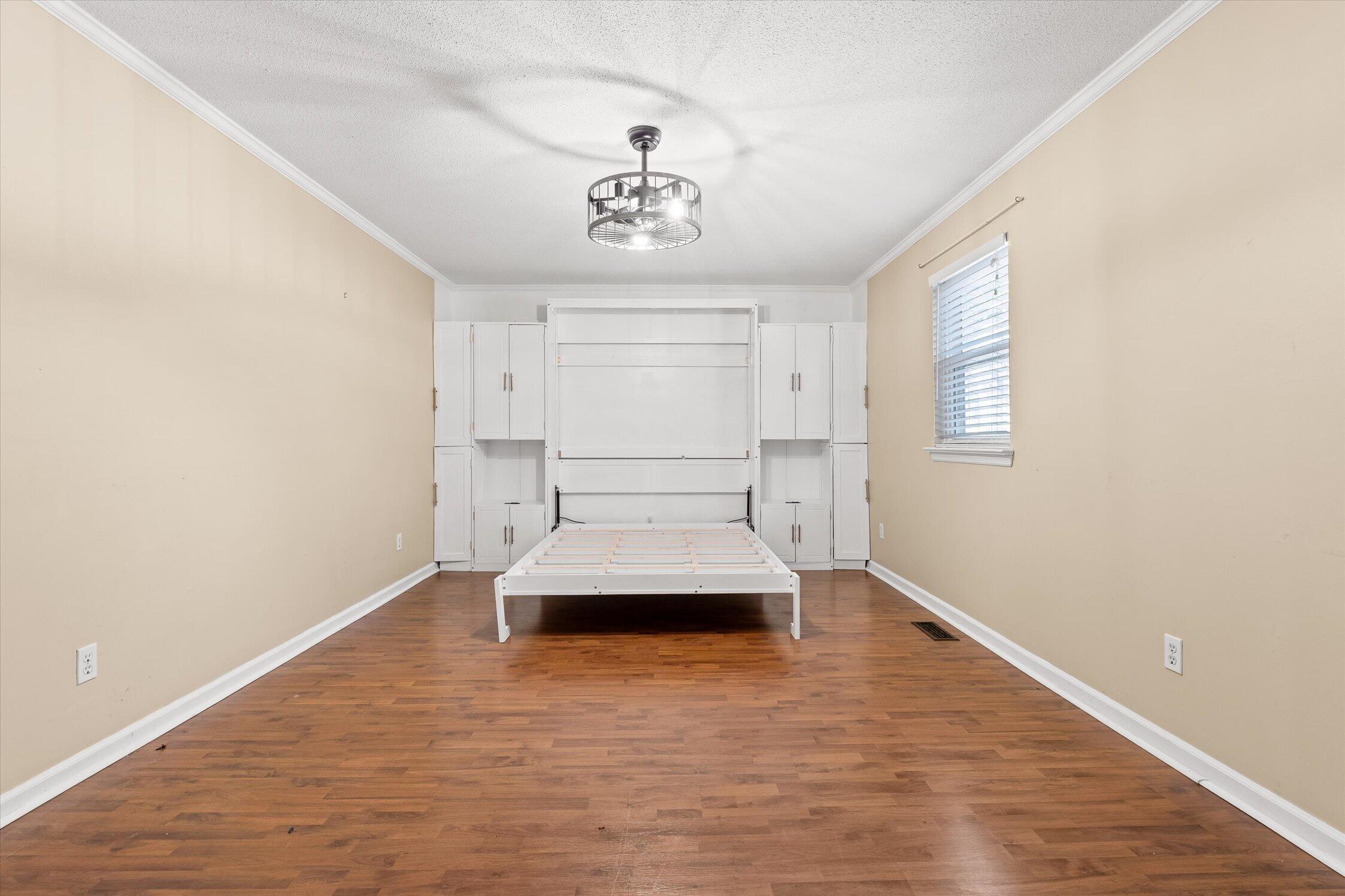 Bedroom with a white Murphy bed frame, built-in cabinets, and hardwood flooring.