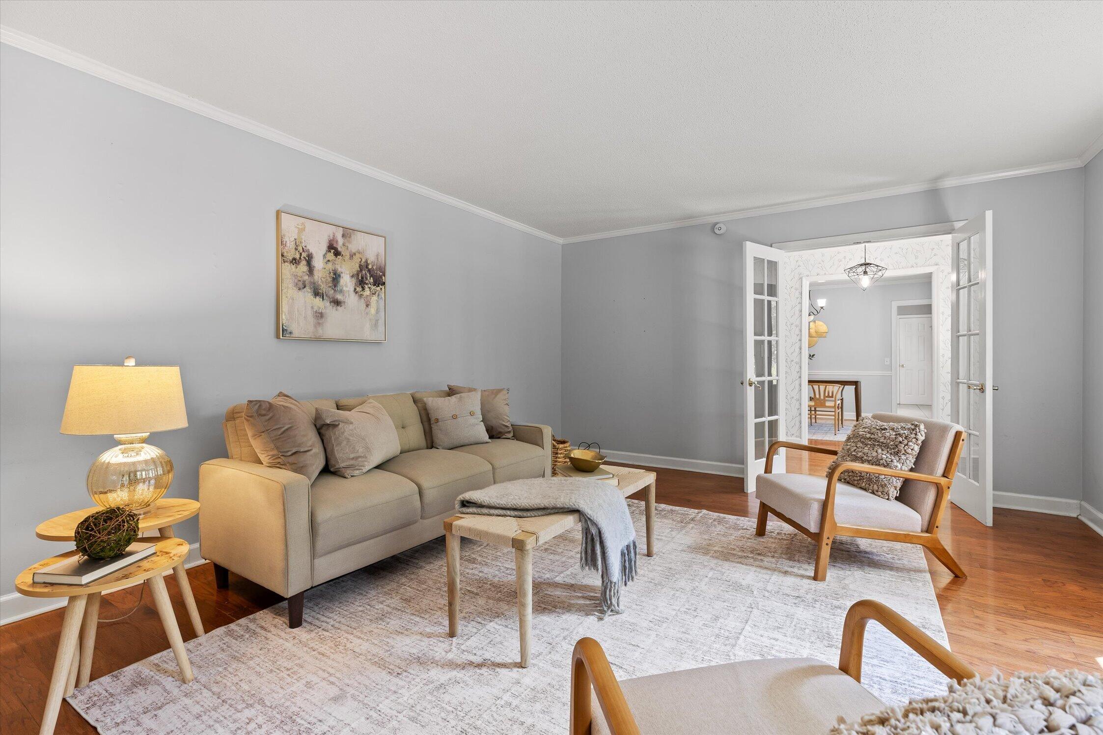 Furnished living room with a beige sofa, pale rug, hardwood floors, and open French doors.