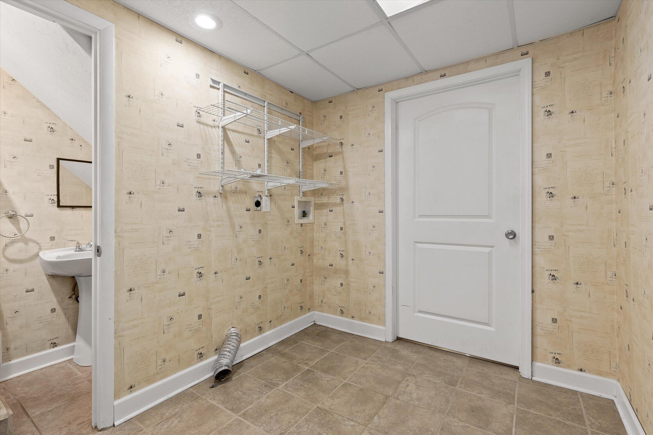 Empty room with wire shelving, patterned wallpaper, tile floor, and a dryer vent hose.