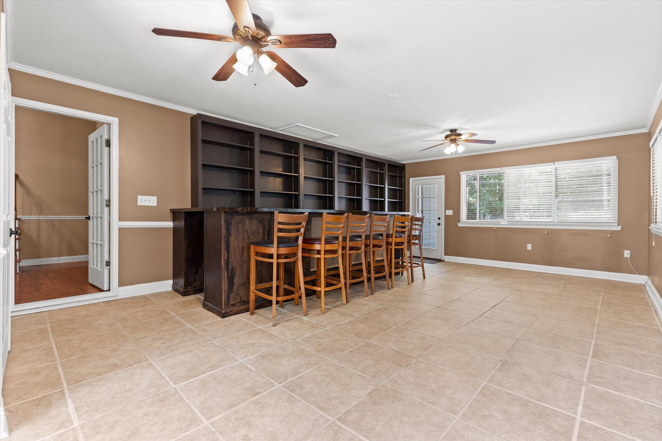 Interior room with built-in shelving, a long bar counter, wooden stools, and large tiled floors.