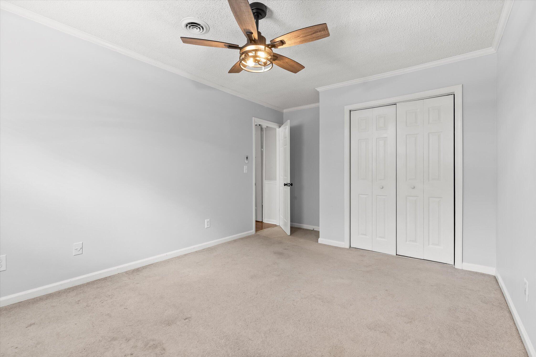 Empty bedroom with beige carpet, a wood-blade ceiling fan, and white sliding closet doors.