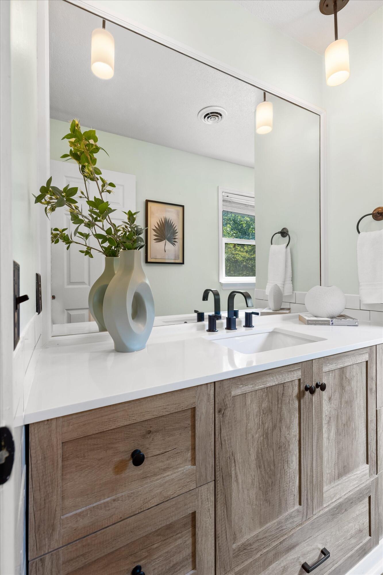 Bathroom vanity with a large mirror, white countertop, black faucets, and rustic wood cabinetry.