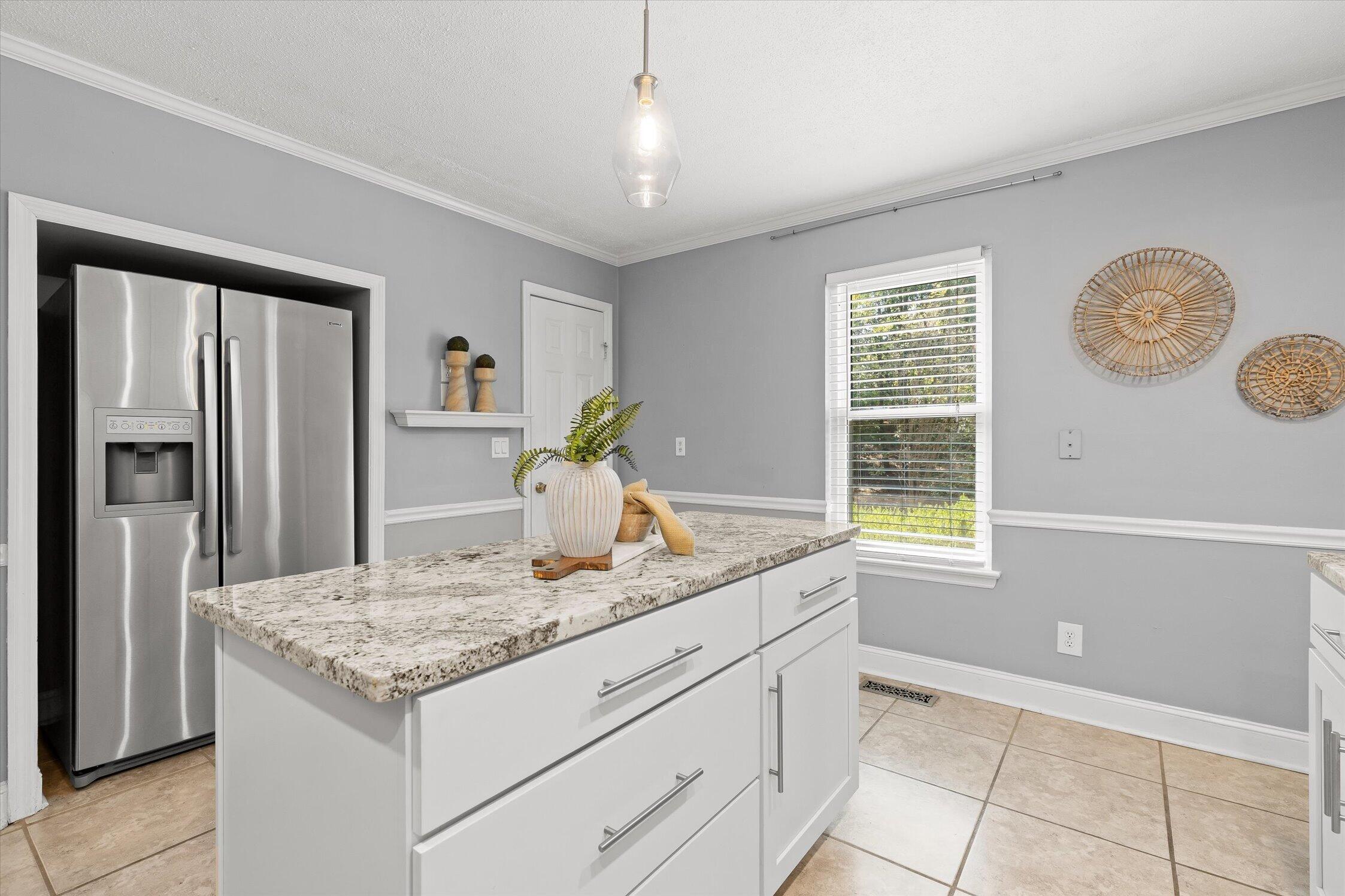 Kitchen with a granite-topped island, white cabinetry, and a stainless steel refrigerator.