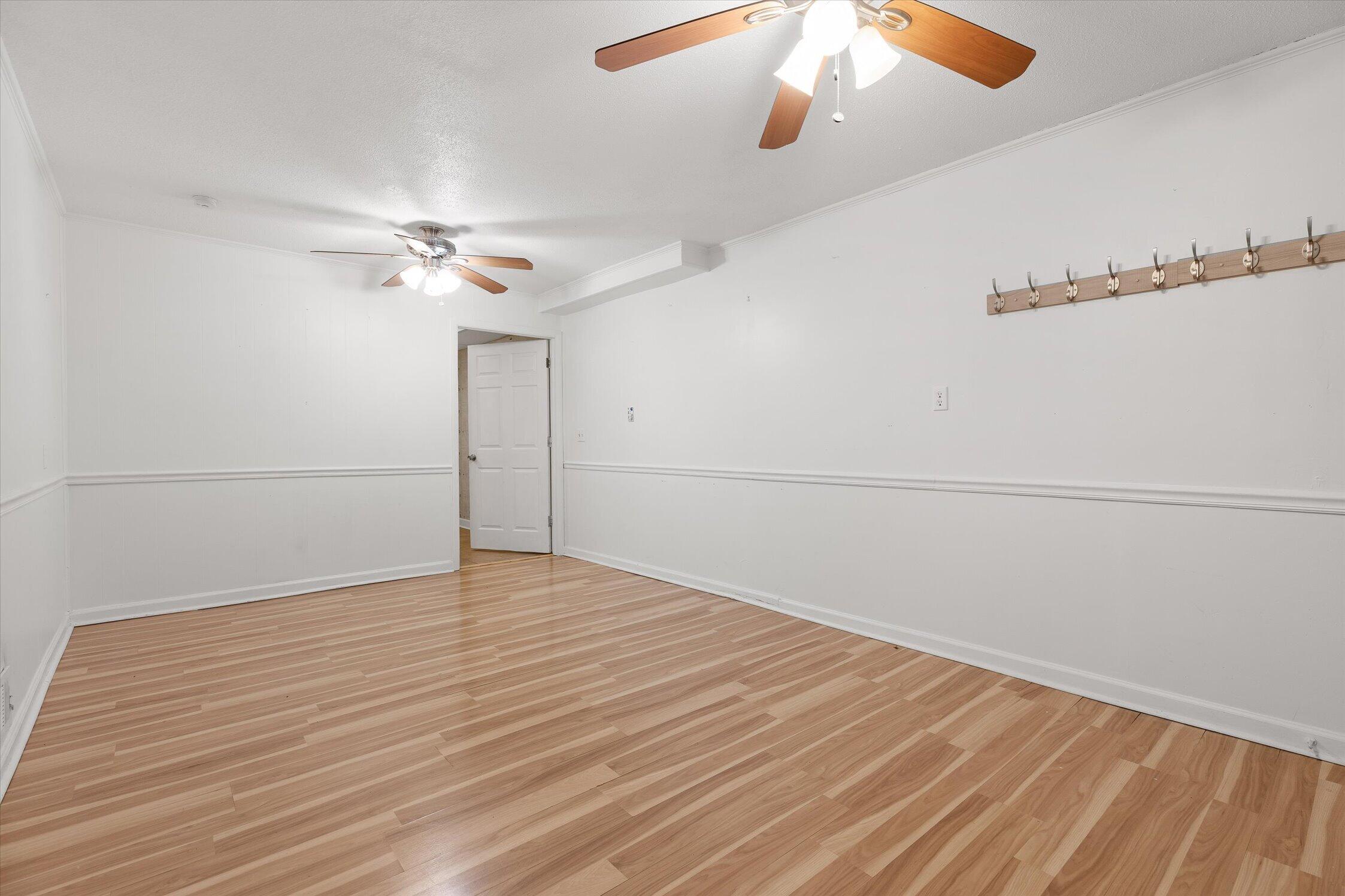 Empty room with light wood-look flooring, white paneled walls, ceiling fans, and wall hooks.