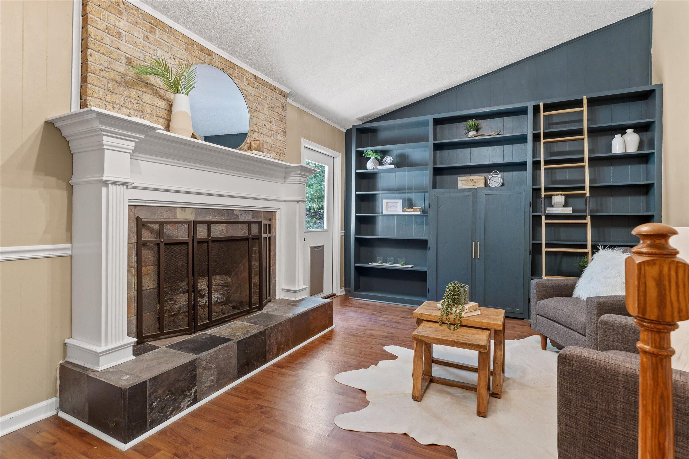 Living room with a stone fireplace, blue built-in bookshelves, rolling ladder, and wood floors.