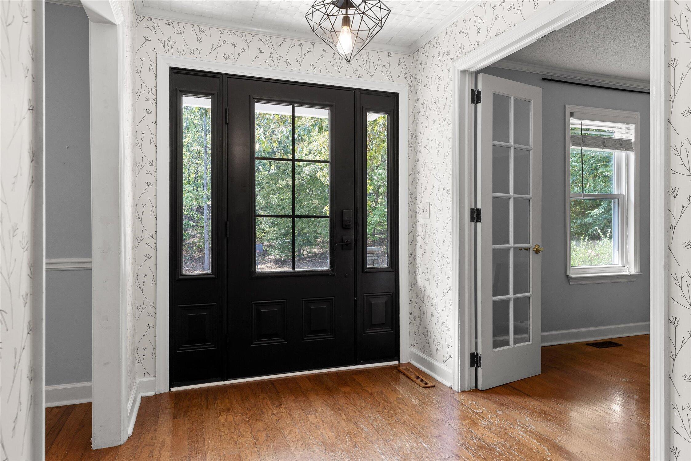 Entry foyer with a black glass-paneled front door, patterned wallpaper, and hardwood floors.