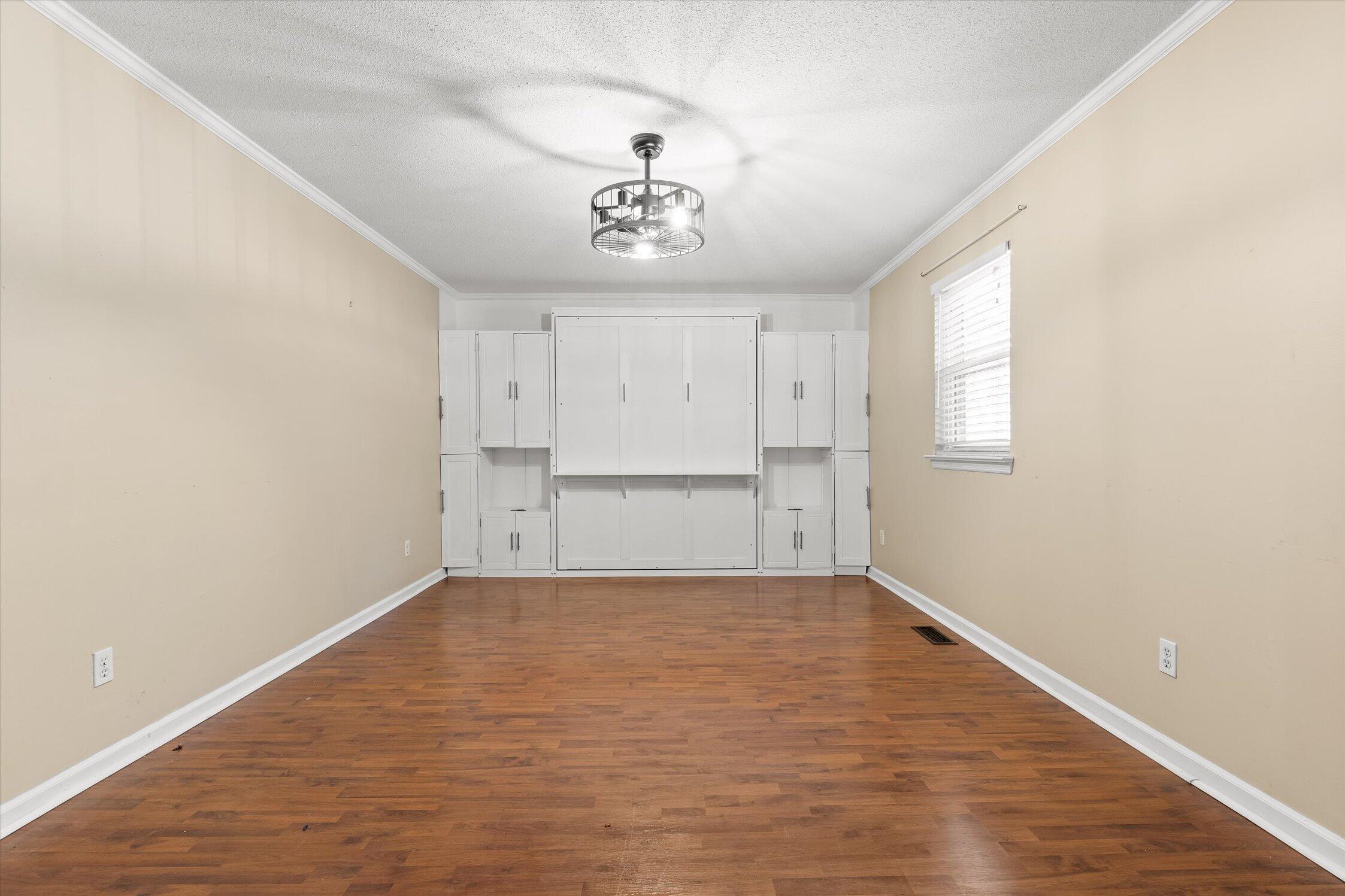Empty bedroom with a built-in white Murphy bed, matching cabinets, and hardwood floors.