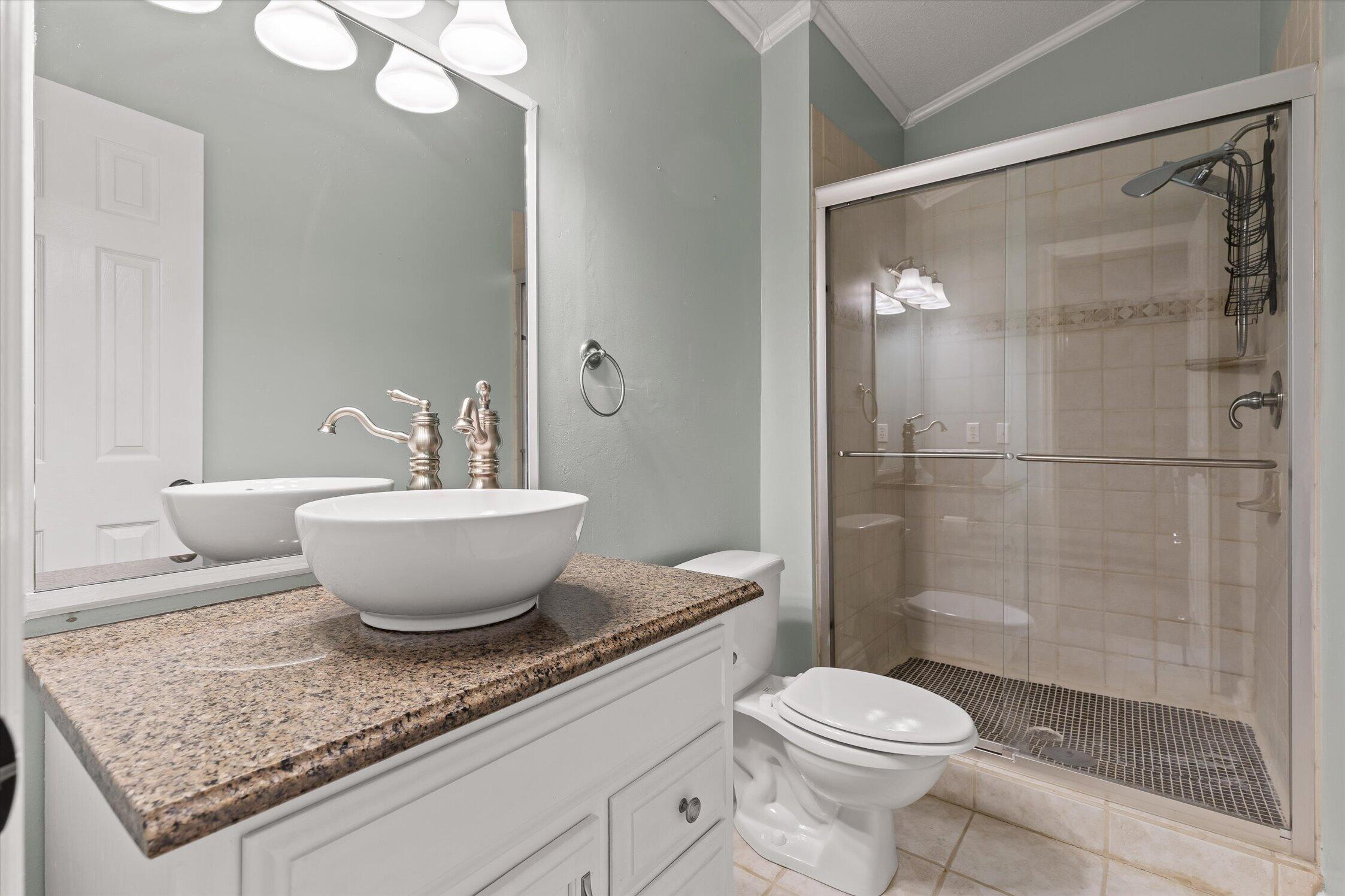 Bathroom with a granite vanity and glass-enclosed tiled walk-in shower.