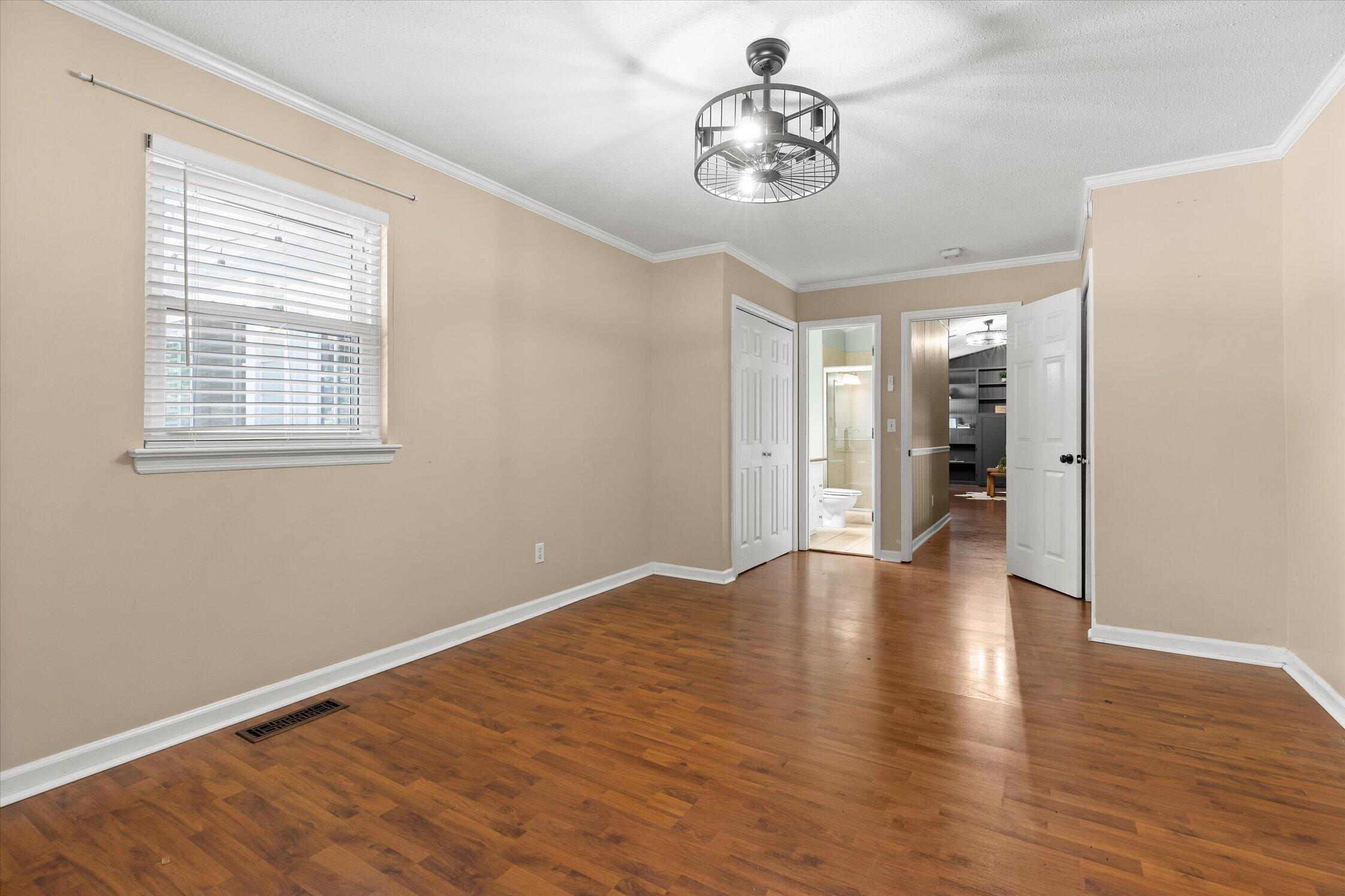 Empty room with hardwood floors and beige walls, opening to a bathroom and a room with built-in shelving.