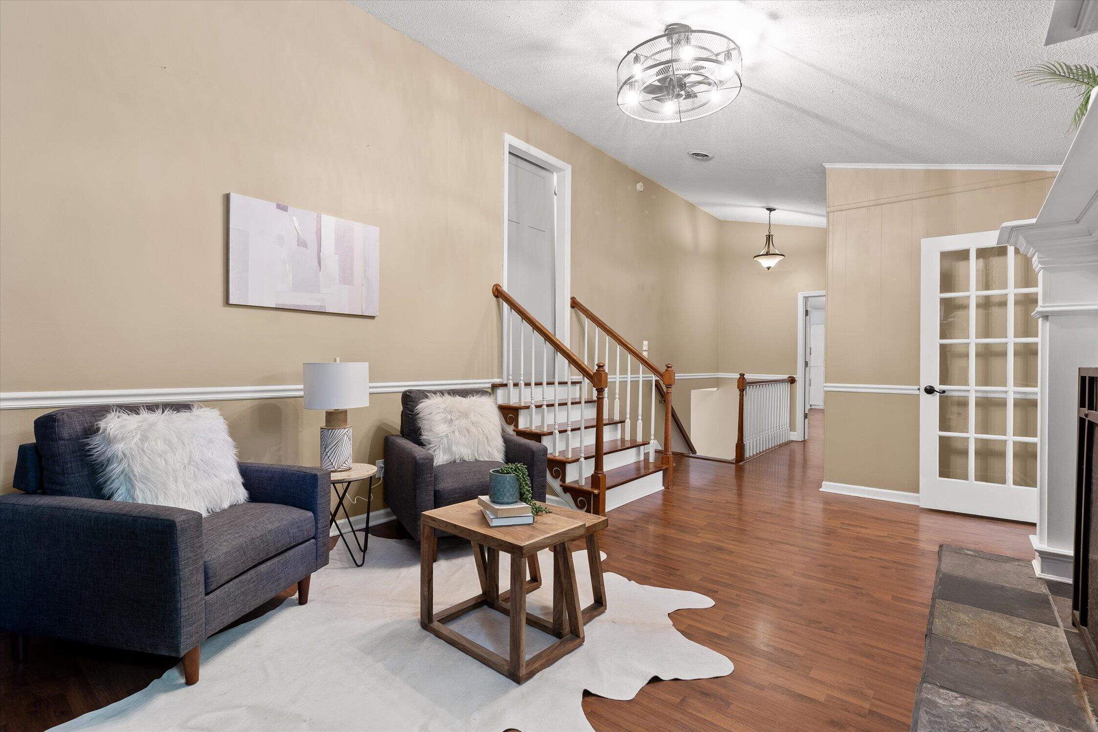 Staged living room with navy seating, hardwood floors, and a staircase with wood handrails.