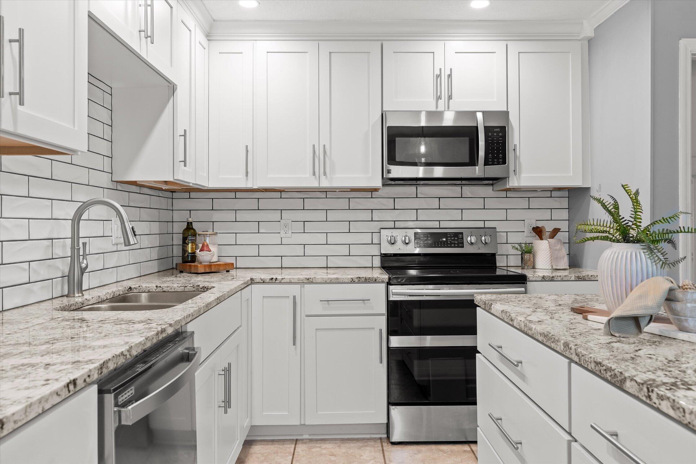 Bright kitchen with white cabinetry, subway-tile backsplash, stone counters, and stainless steel appliances.