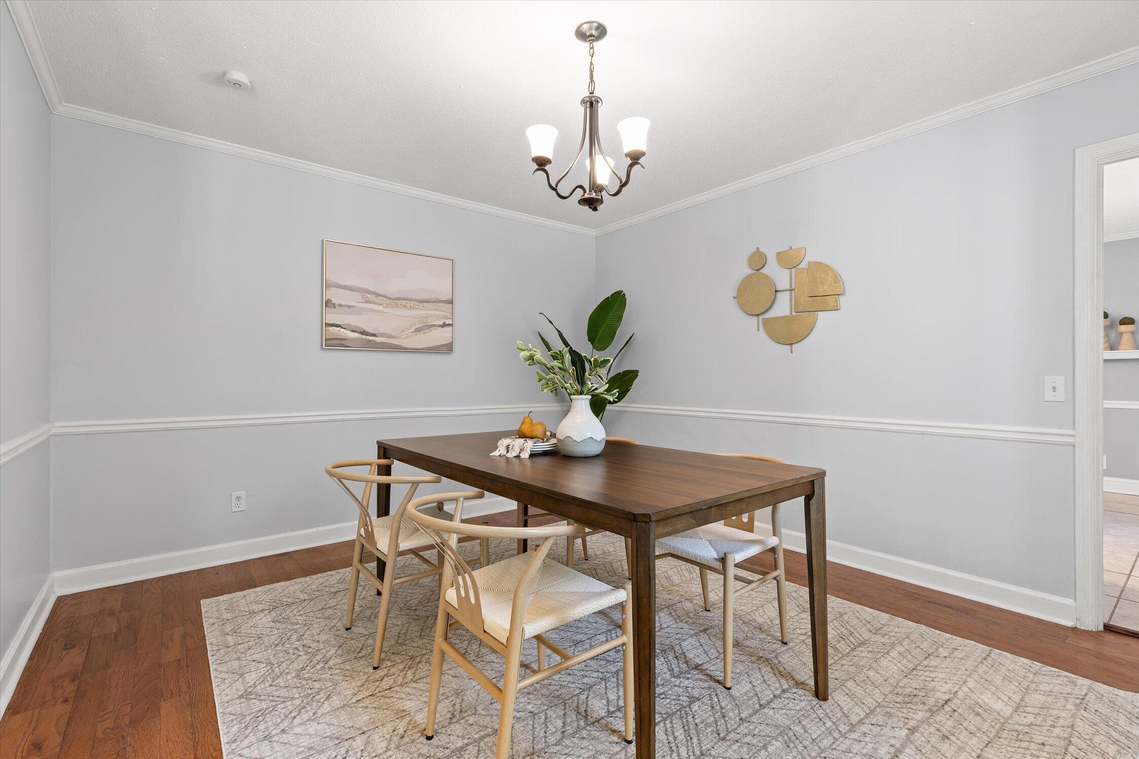 Staged dining room with a dark wood table, woven chairs, patterned rug, and chandelier.