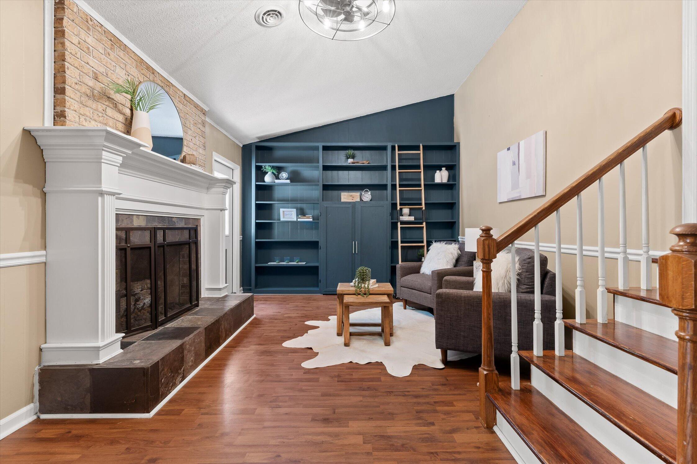 Living room with a brick-surround fireplace, dark built-in shelves and ladder, and a wooden staircase.