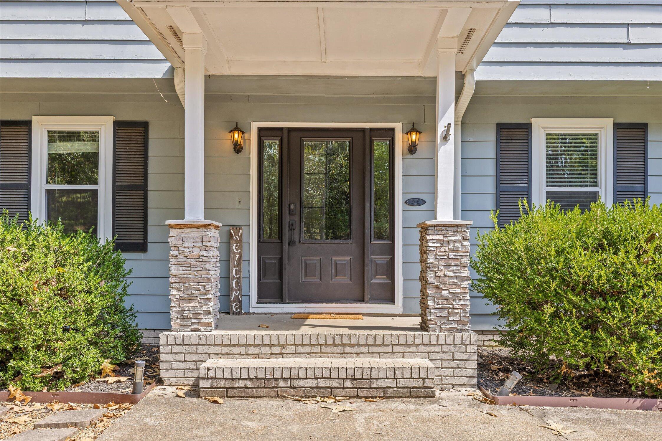 Front porch with a dark paneled door, stone columns, and blue-gray siding.