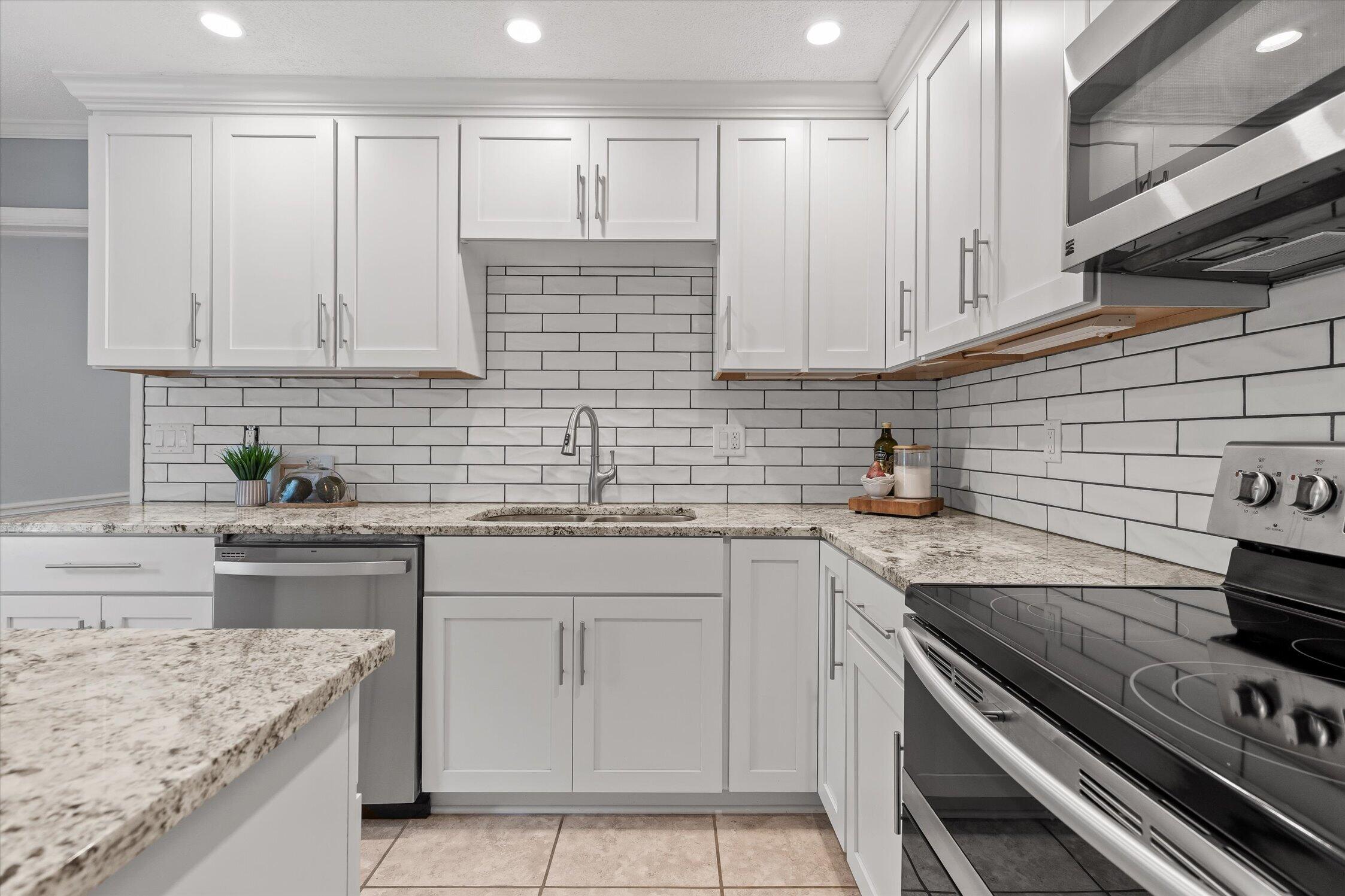 Renovated kitchen with white cabinets, subway tile backsplash, stone counters, and stainless steel appliances.