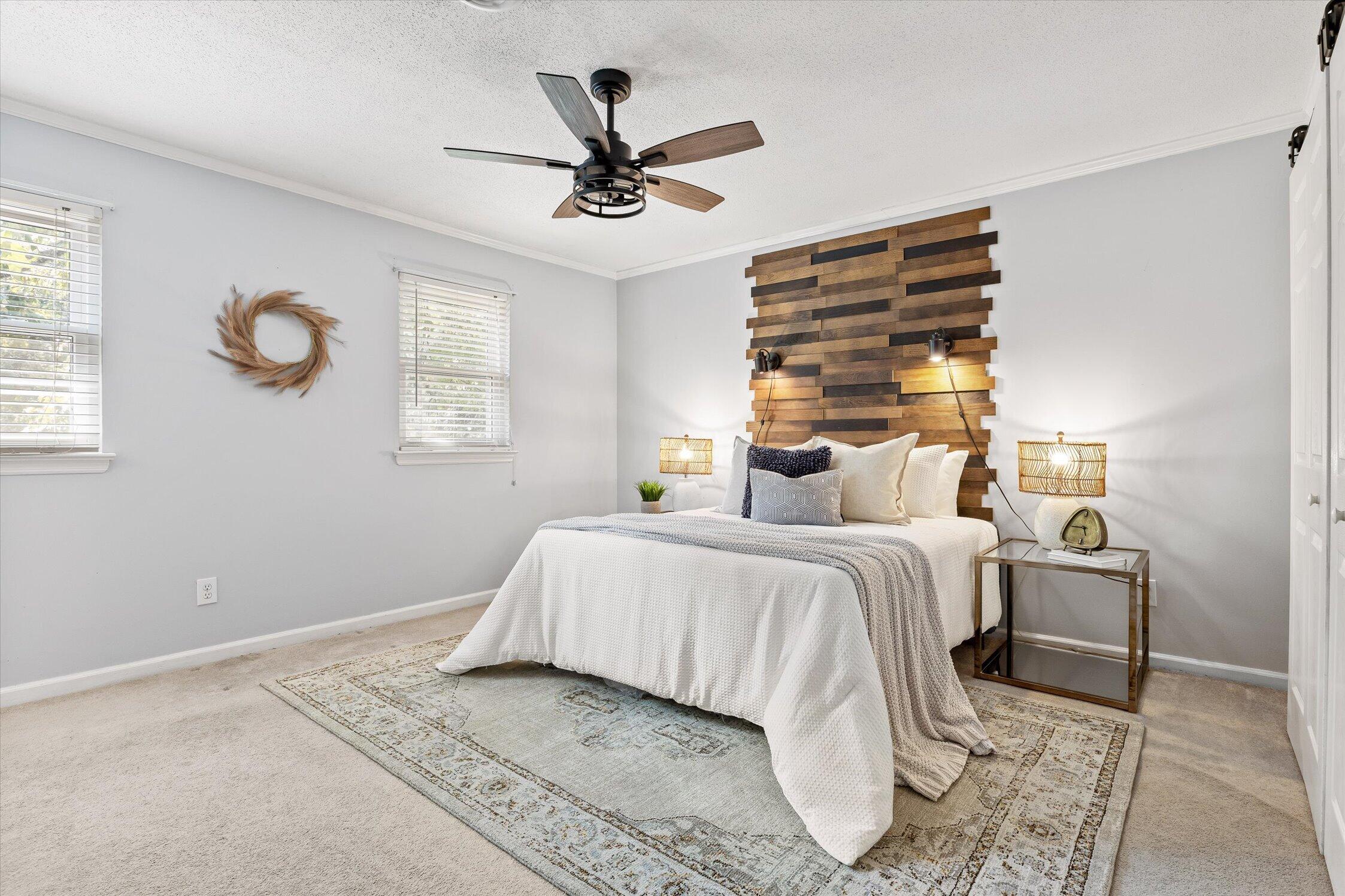 Staged bedroom with a white bed, wood-plank accent wall, and two windows with blinds.