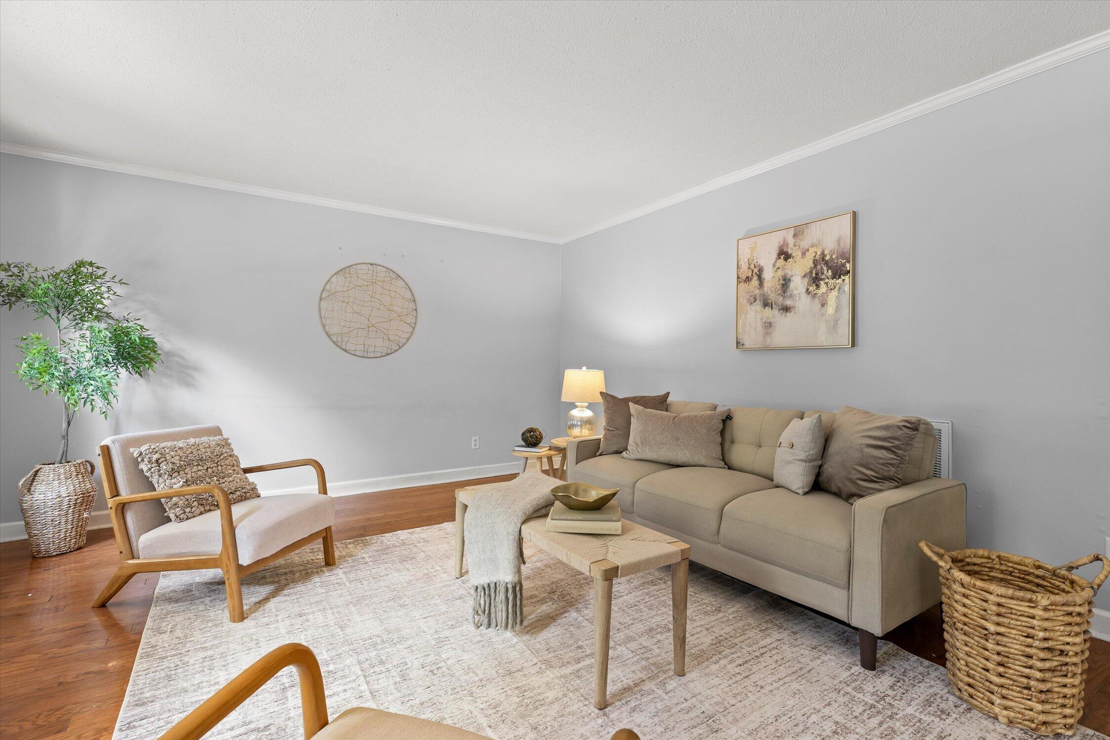 Staged living room with a beige sofa, wooden armchair, and light patterned rug.