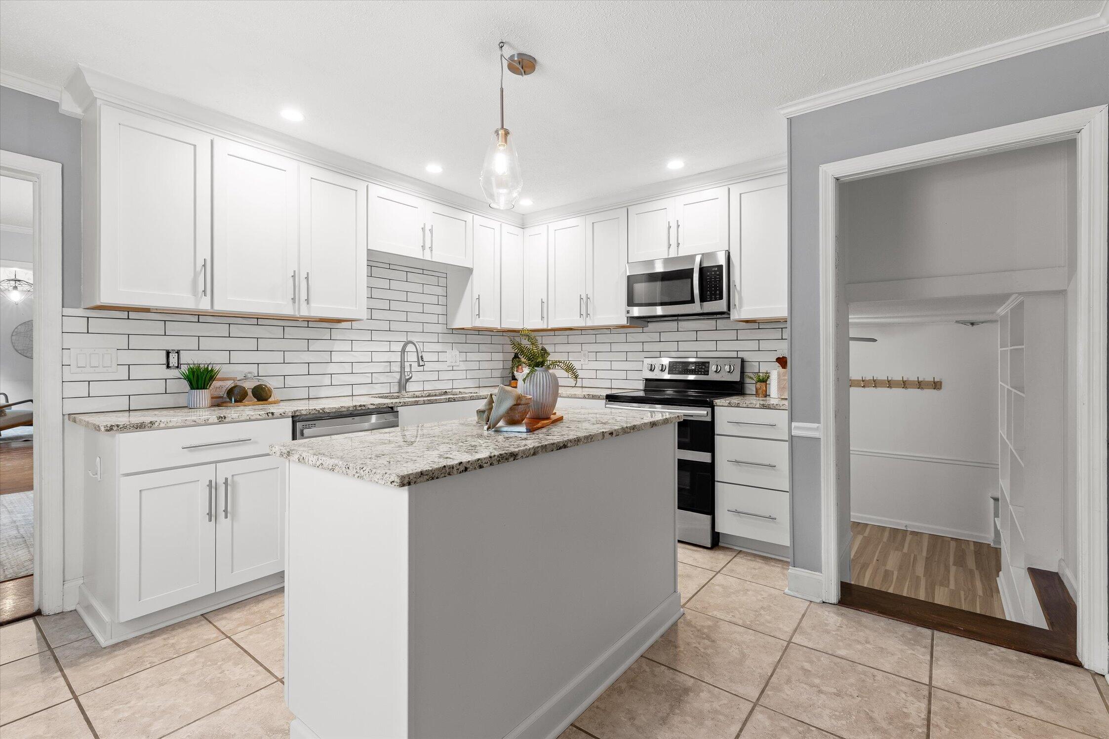 Kitchen with white shaker cabinets, granite island, subway tile backsplash, and stainless steel appliances.