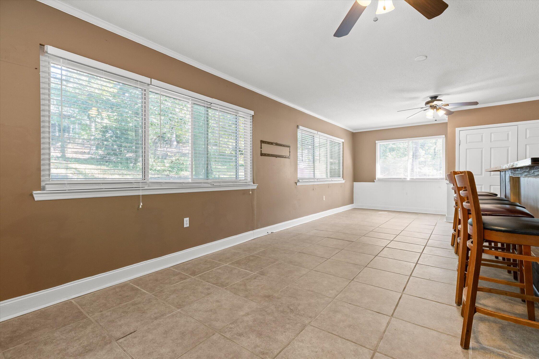 Dining area with tiled floors, wide windows, and wooden bar stools beside the kitchen island.