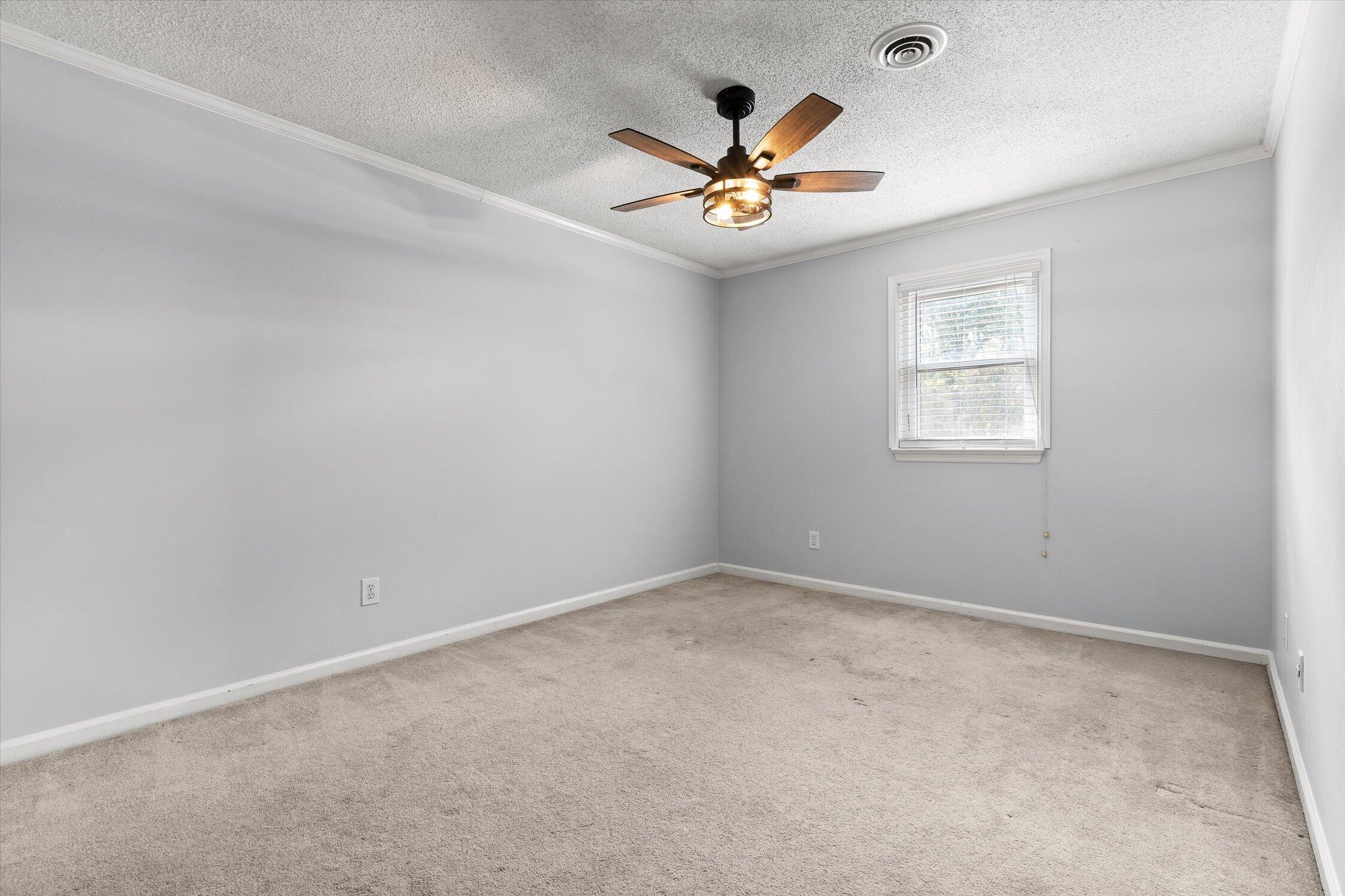 Empty carpeted room with gray walls, a window with blinds, and a lit ceiling fan.