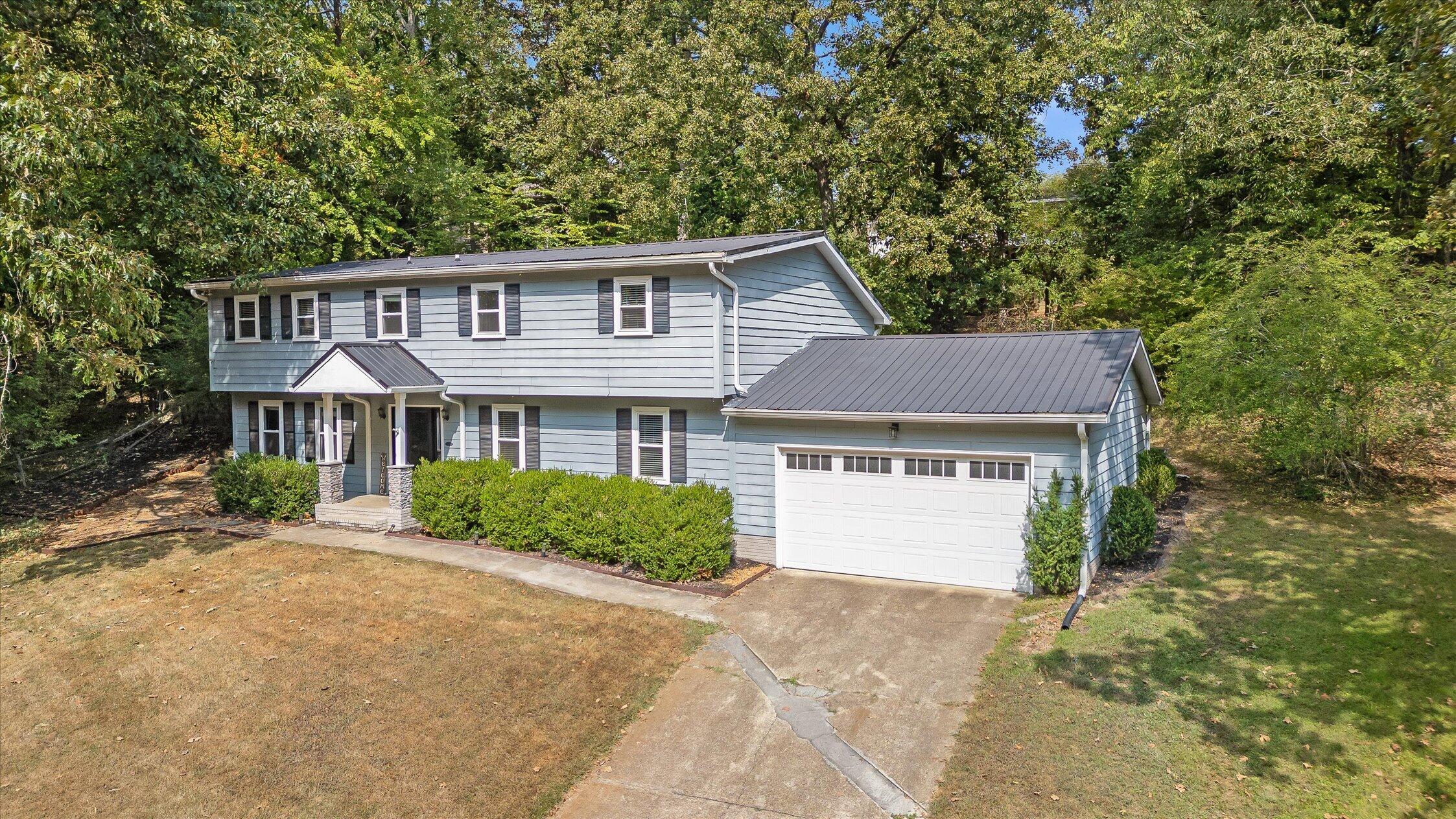 Two-story blue house with a metal roof, attached garage, and mature trees.