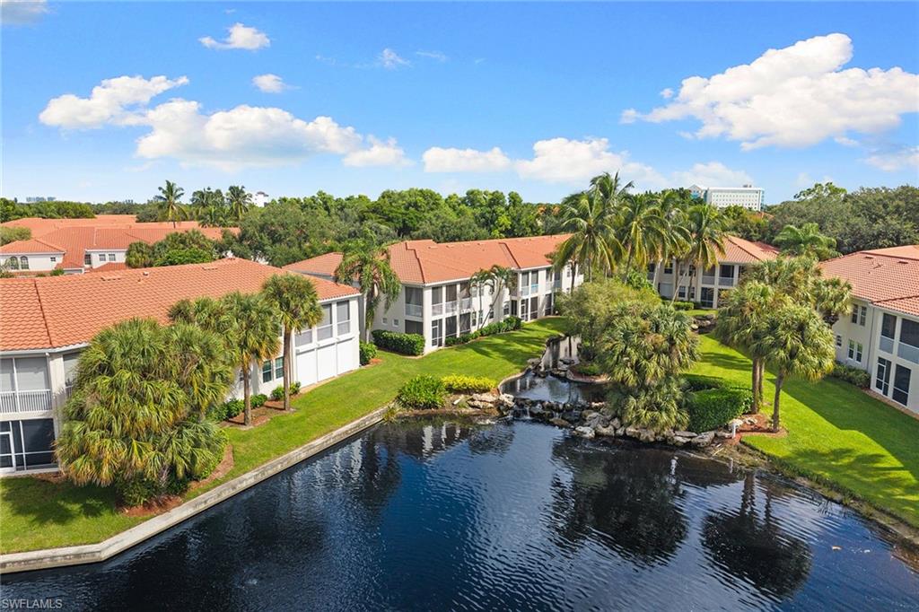 Aerial view of tropical condominium buildings surrounding a landscaped pond and waterfall.