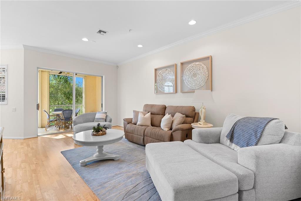 Furnished living room with a gray sectional, brown sofa, and sliding doors to a leafy balcony.