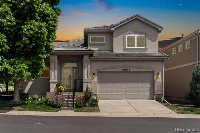 Two-story gray stucco home with a double garage, landscaped entry, and large leafy tree.