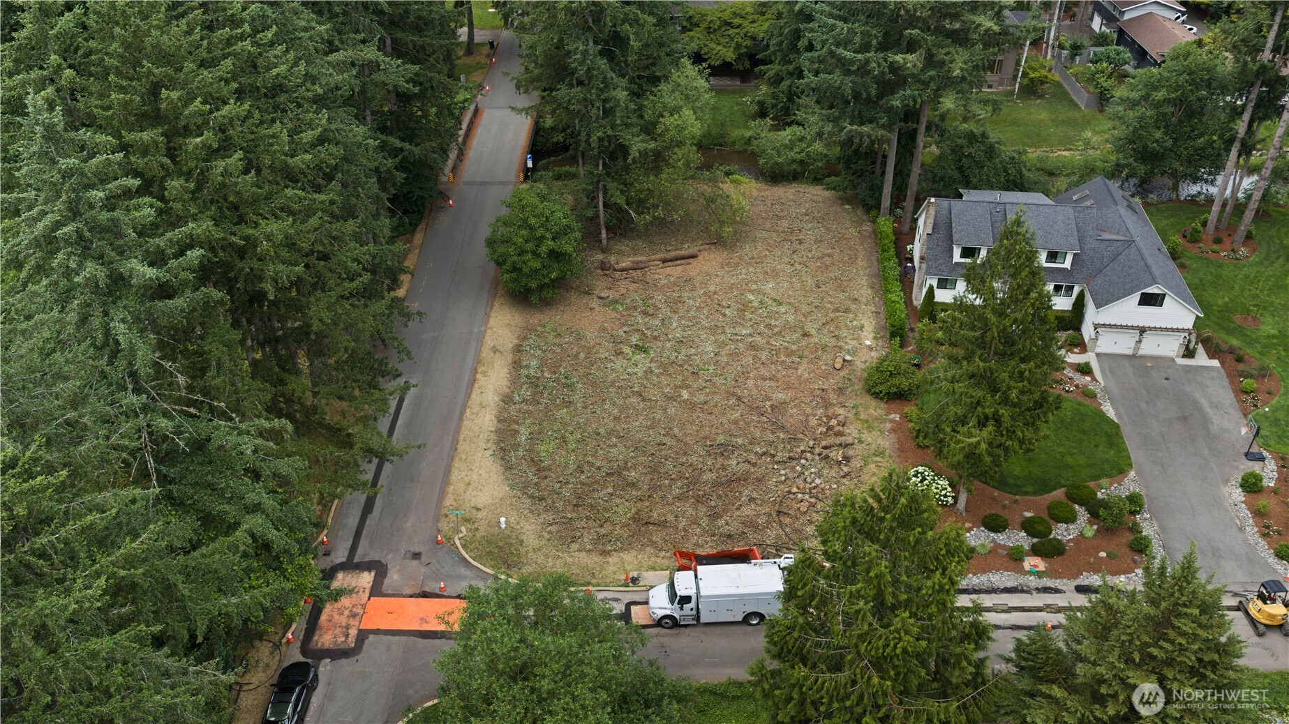 Aerial view of a cleared vacant lot bordered by mature trees and a residential road.