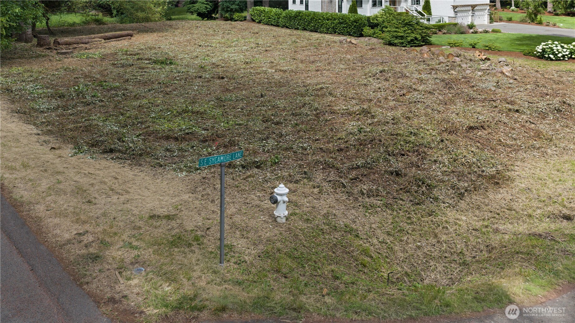 Cleared residential lot with a SE Sycamore Lane sign and fire hydrant in front.