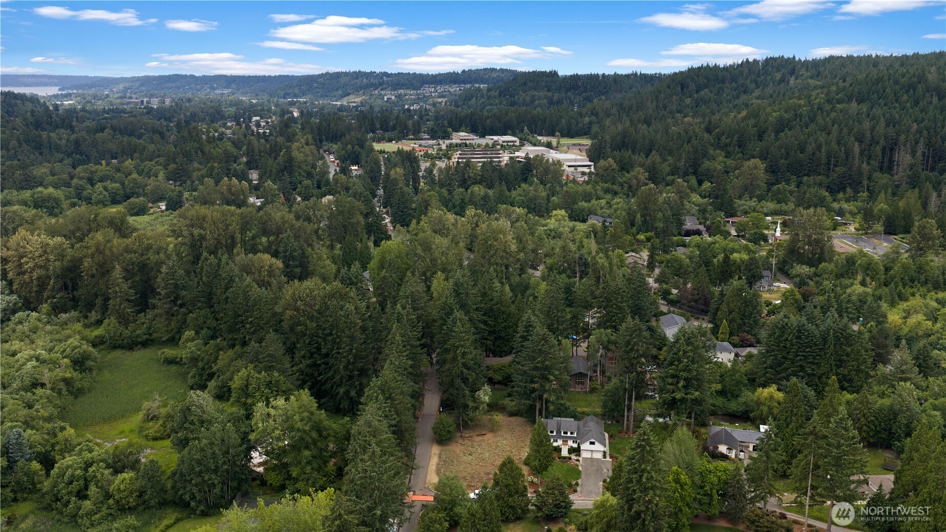 Aerial view of a vacant lot among wooded homes, with a distant lake.
