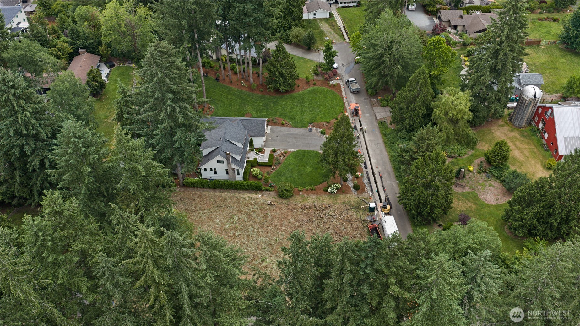 Aerial view of a home surrounded by mature trees, landscaped lawns, and a large cleared area.