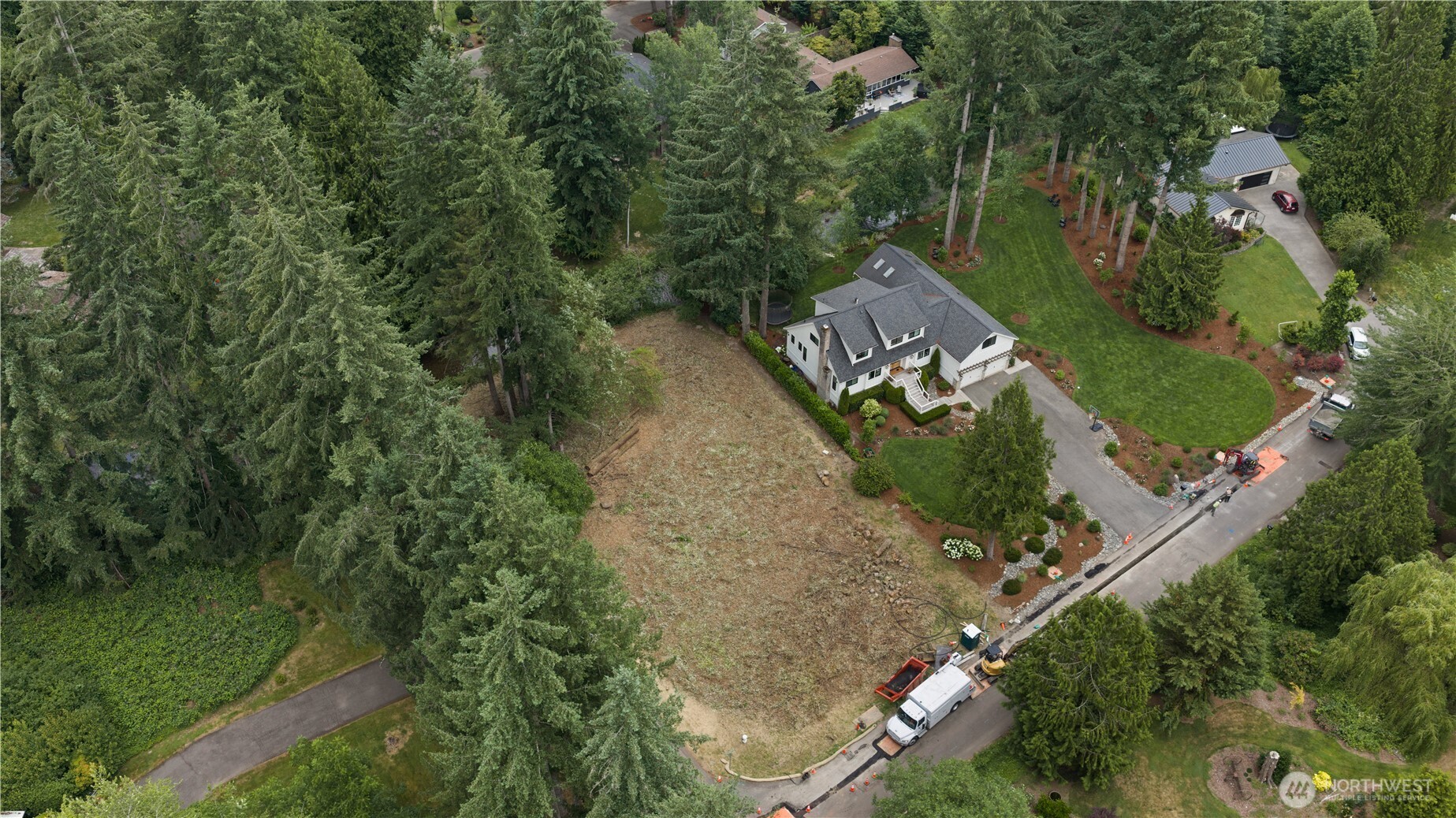 Aerial view of a house beside a large cleared lot, surrounded by evergreen trees.