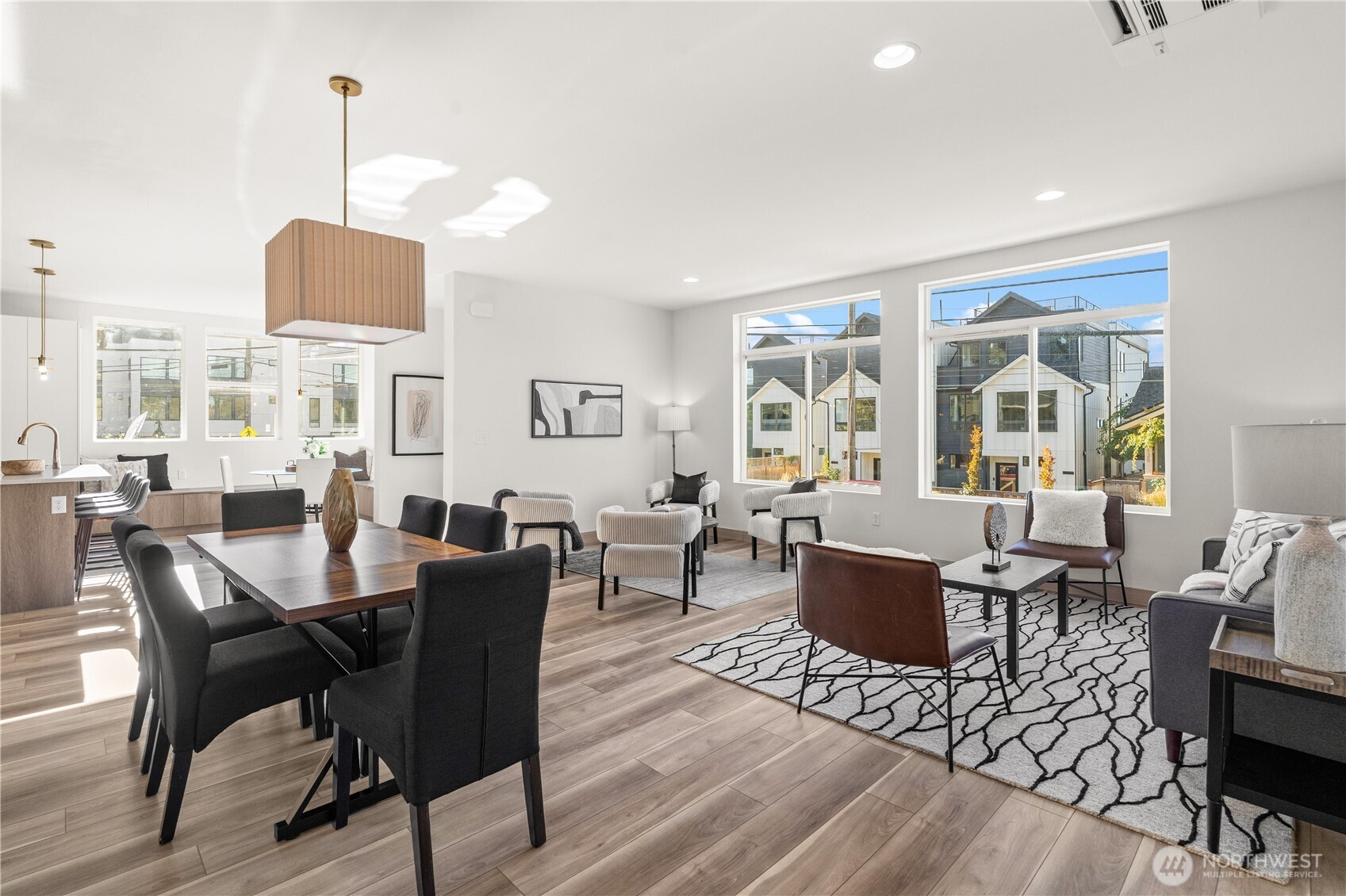 Open-plan living and dining area with large windows, contemporary furnishings, and wood flooring.