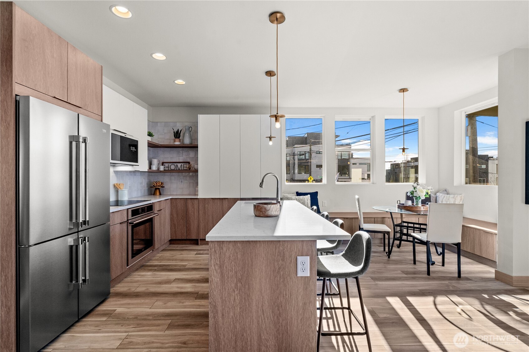 Open-plan kitchen with a large island, wood cabinetry, and dining area beside sunny windows.