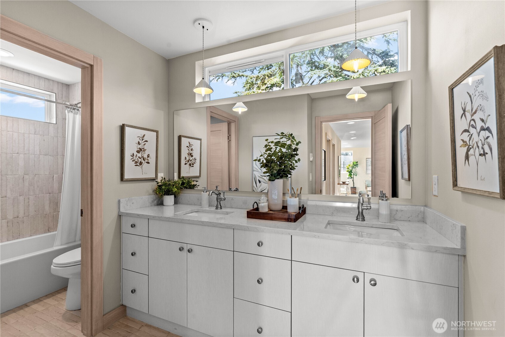 Bathroom with a double-sink vanity, wide mirror, and high windows overlooking leafy trees.