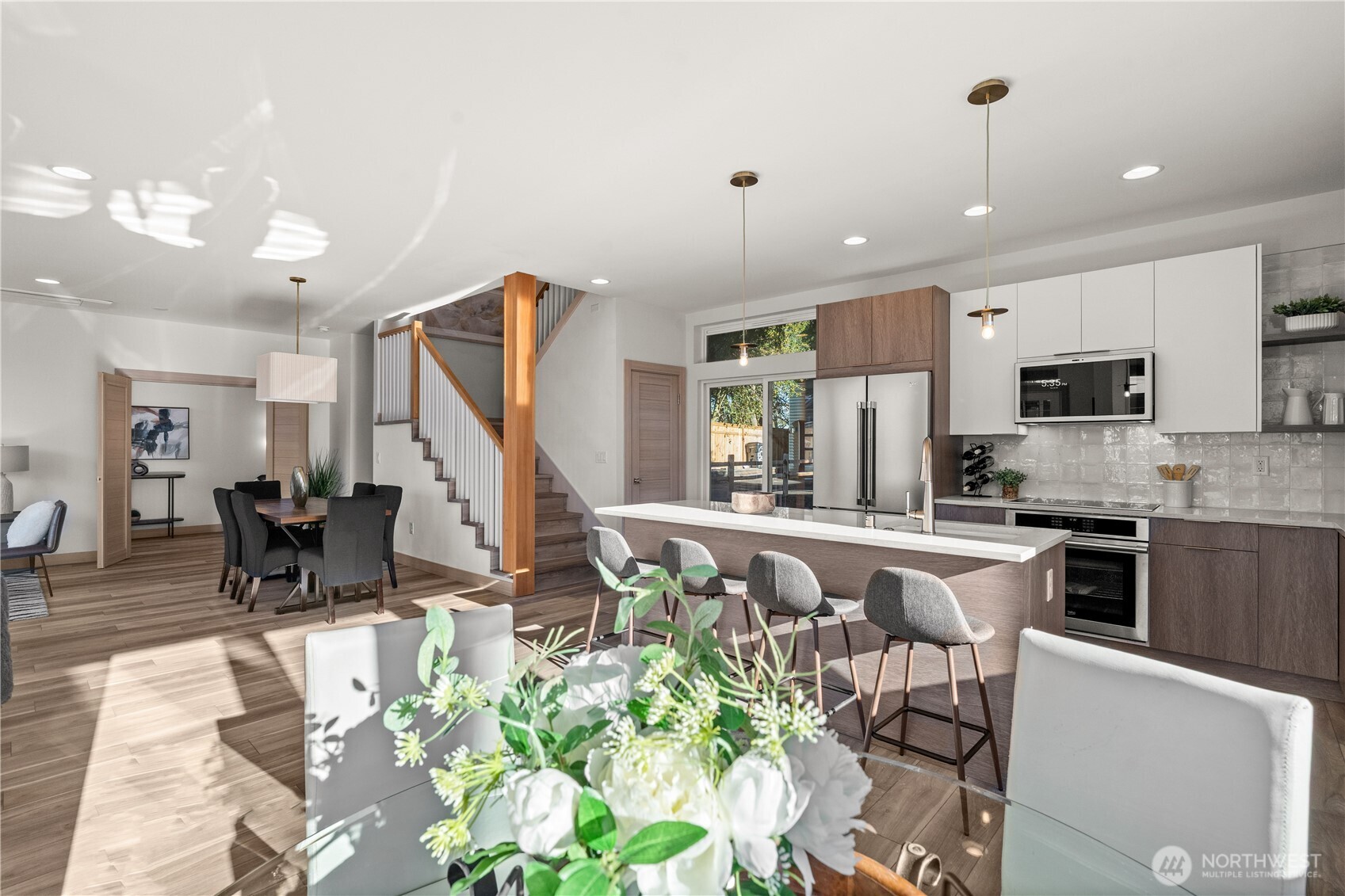 Open kitchen with a large island, stainless steel appliances, and a wood-accented staircase beside the dining area.