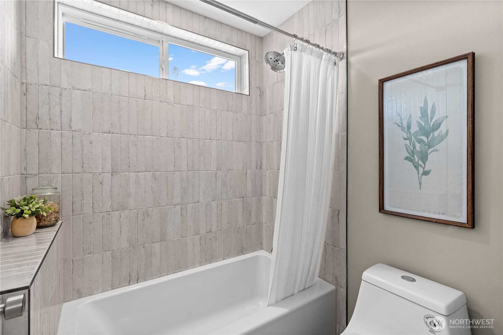Bathroom with a tiled tub and shower beneath a high window.