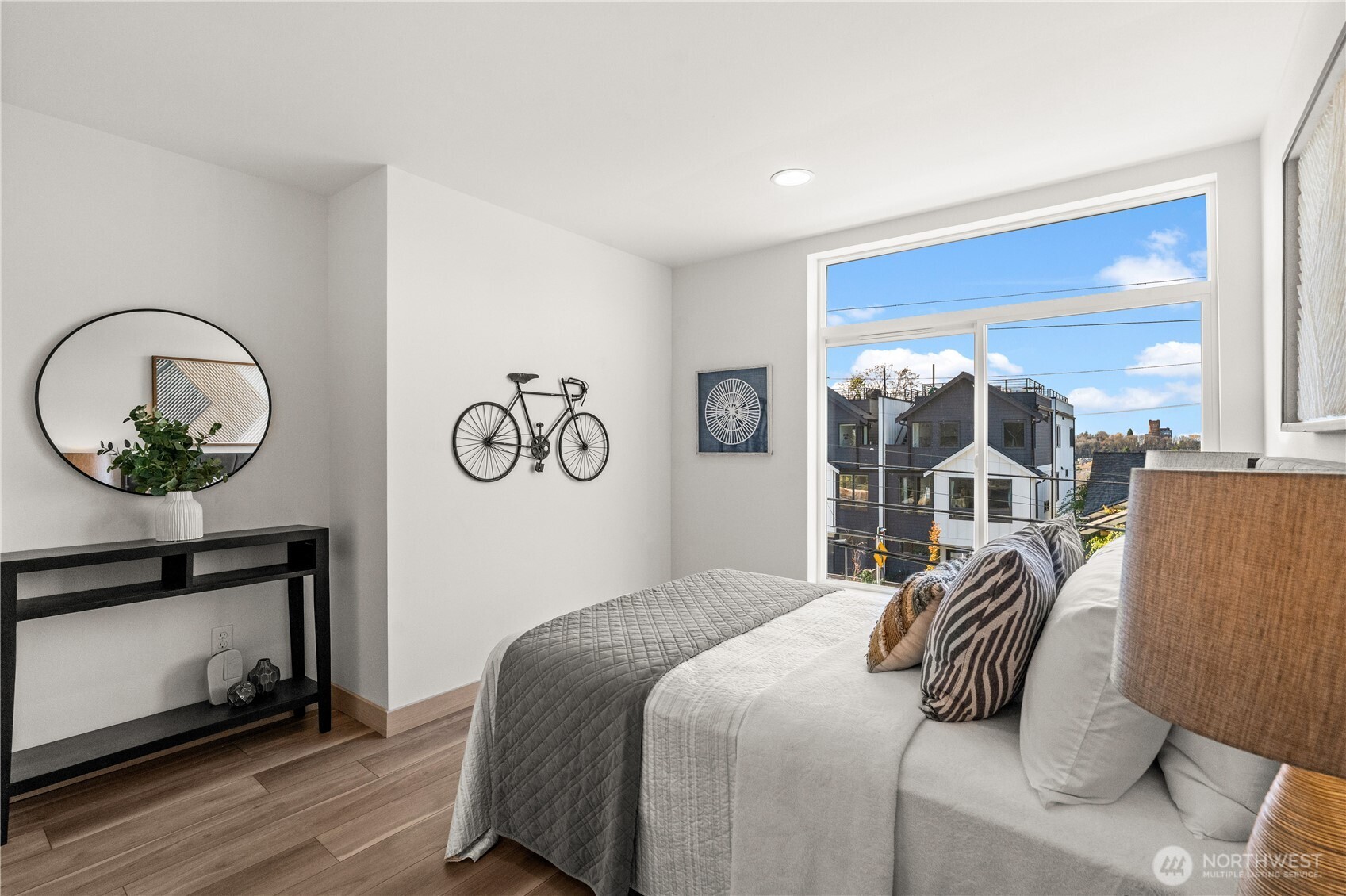 Furnished bedroom with a large window overlooking neighboring homes and bicycle wall decor.