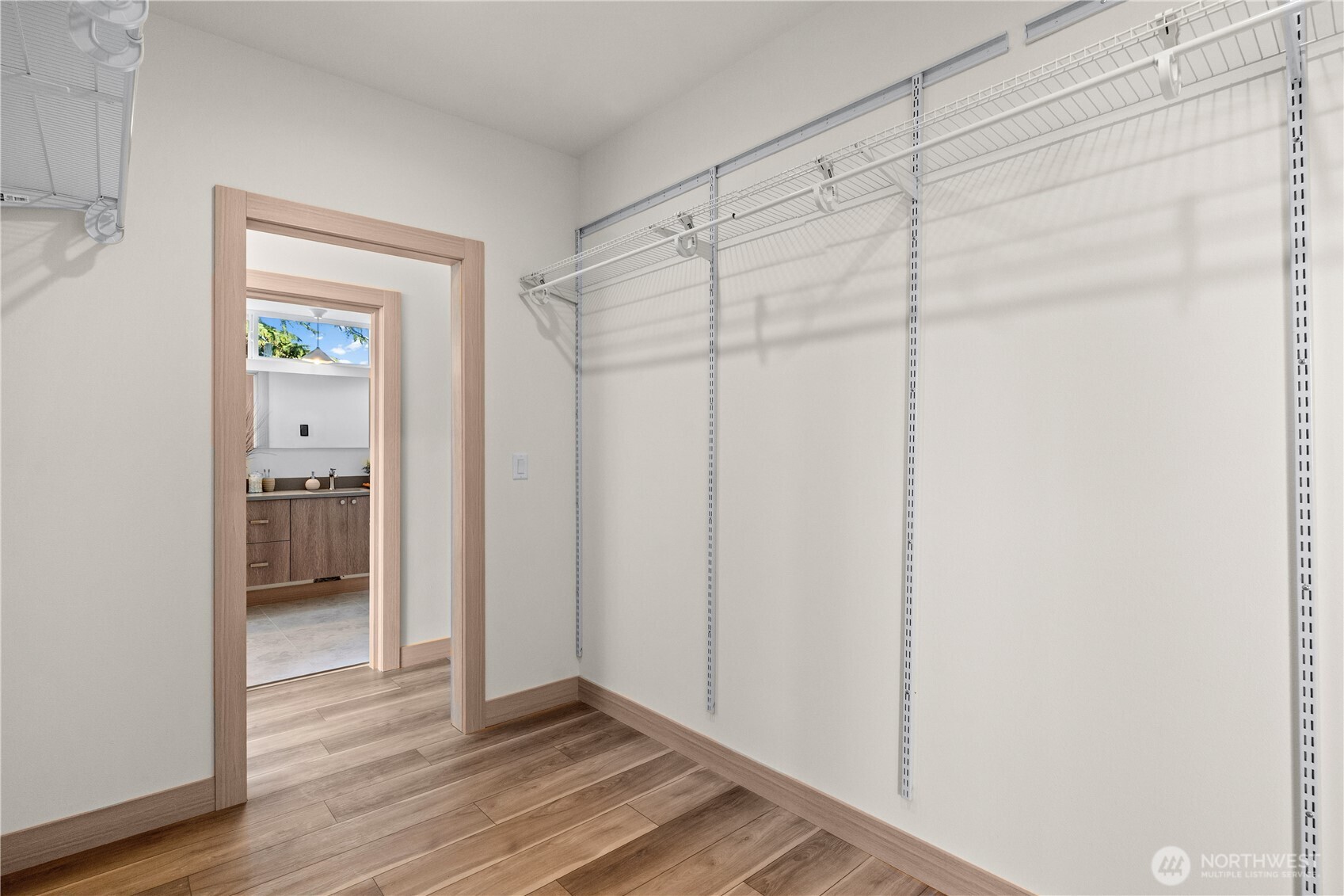 Walk-in closet with white wire shelving and wood flooring, opening to a bathroom vanity.