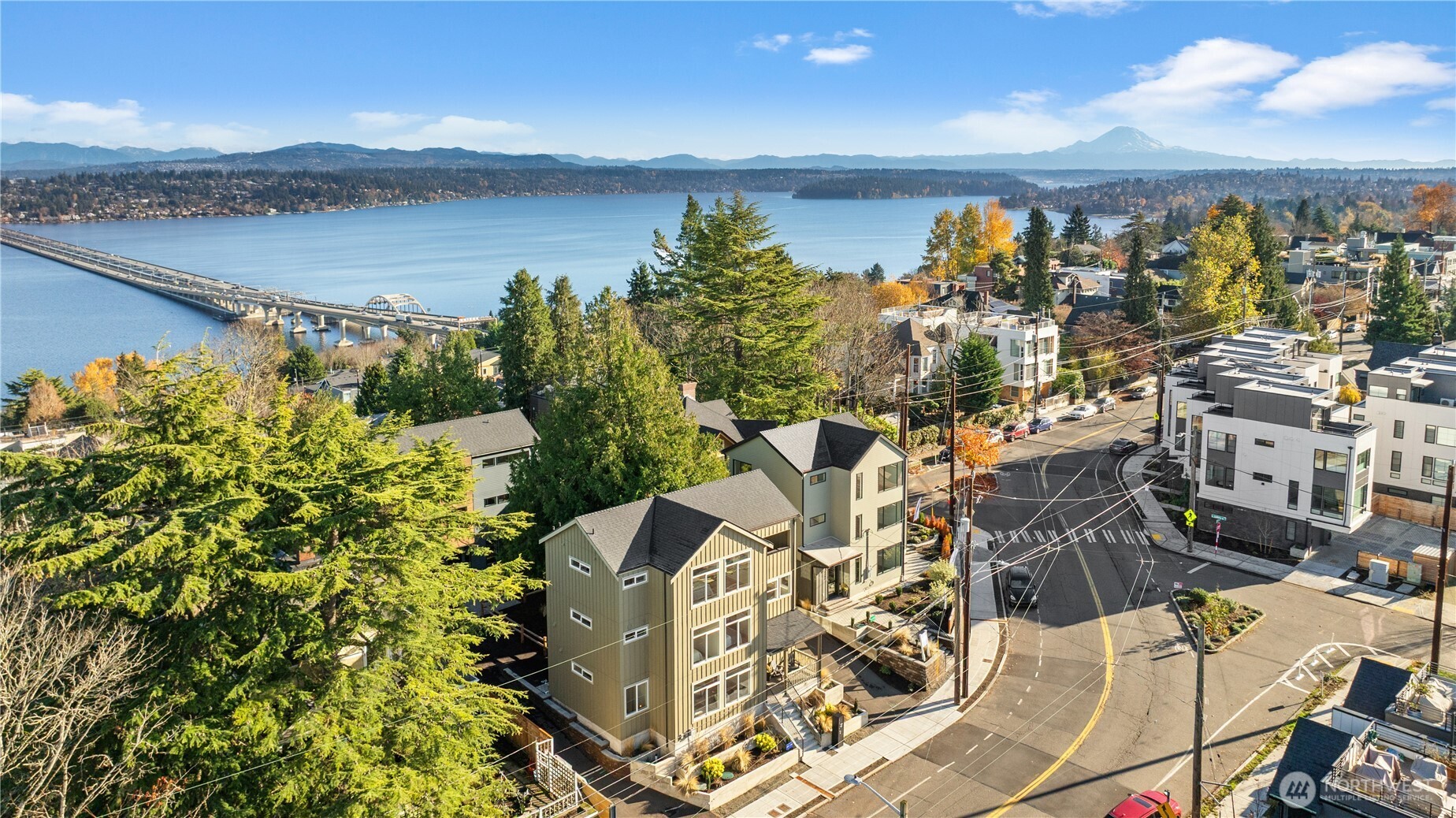 Aerial view of homes above Lake Washington, with a bridge and Mount Rainier beyond.